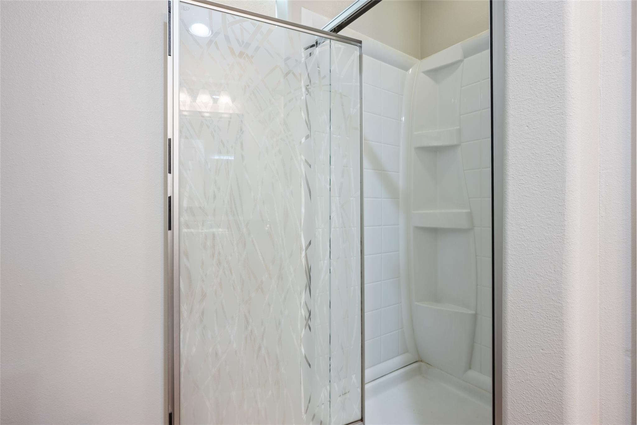 White-tiled shower with a patterned glass door and built-in corner shelves.