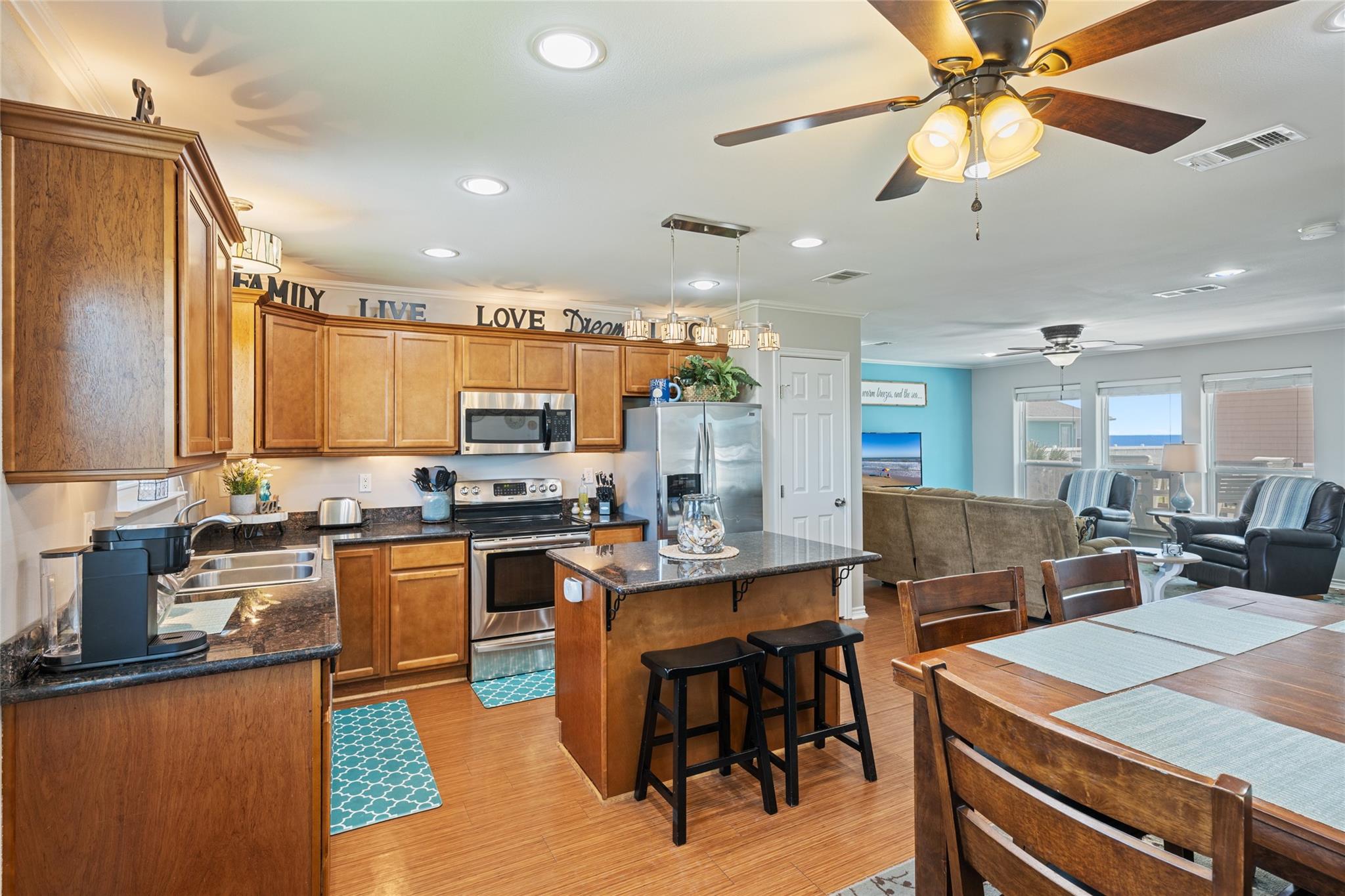 Open-plan kitchen with wood cabinetry and island, adjoining a dining and living area with water visible through windows.