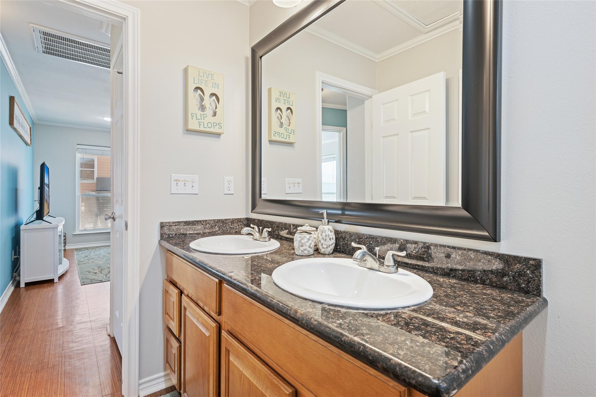 Bathroom double vanity with dark granite counters, wood cabinets, and a large framed mirror.