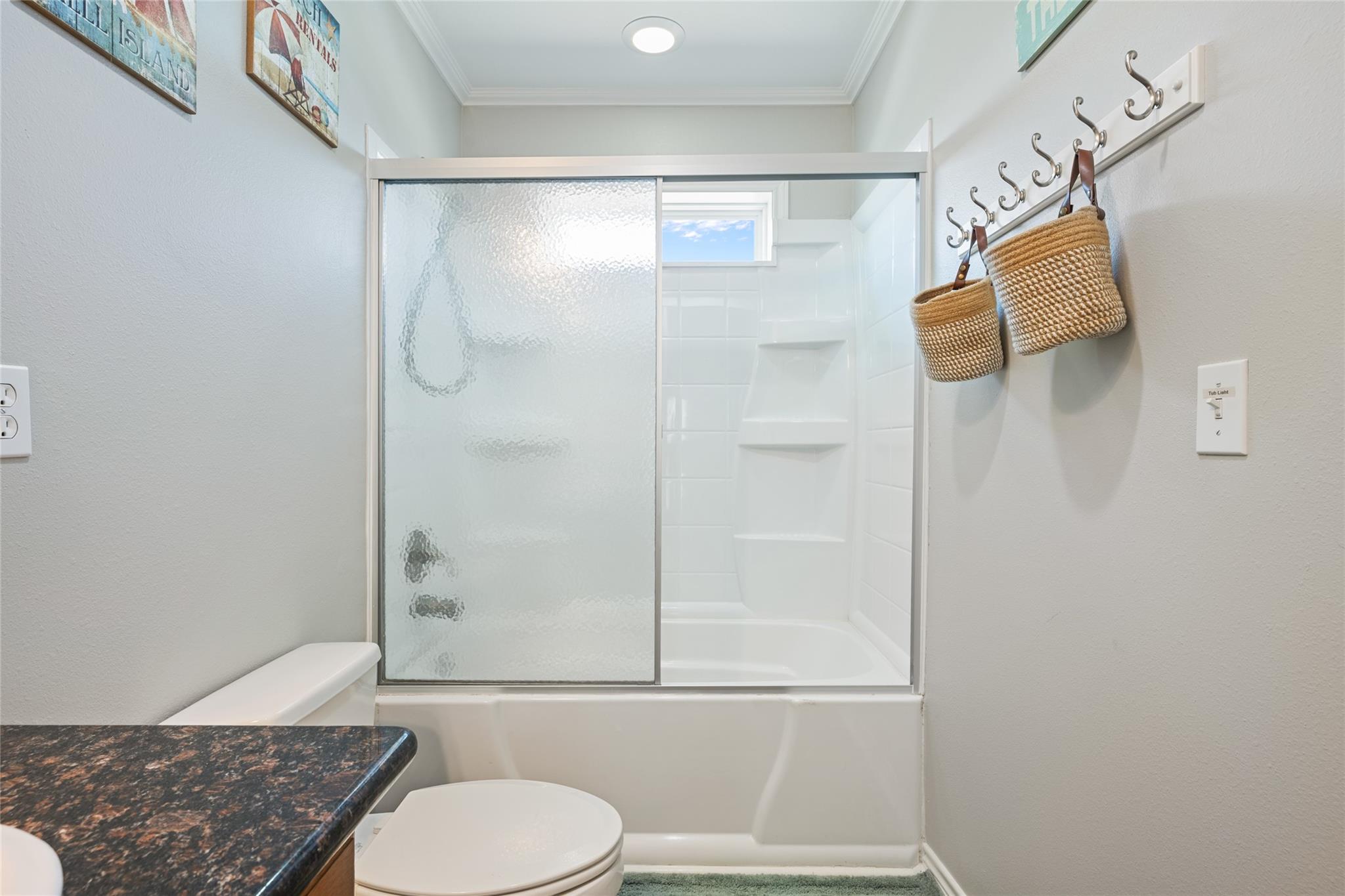 Bathroom with a white tub and frosted sliding shower doors beside a dark granite vanity.