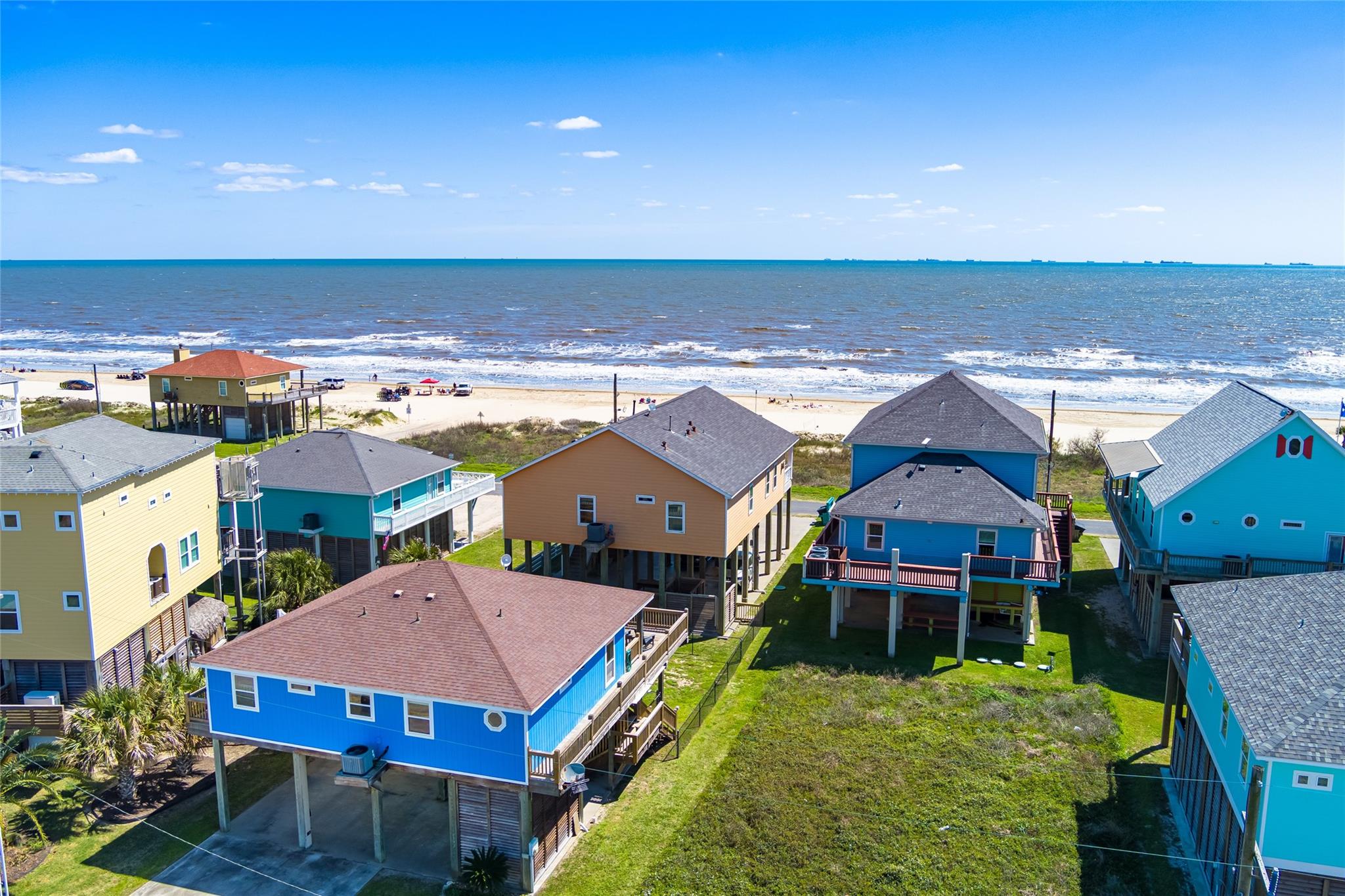 Aerial view of colorful raised beach houses beside the sandy shore and ocean.
