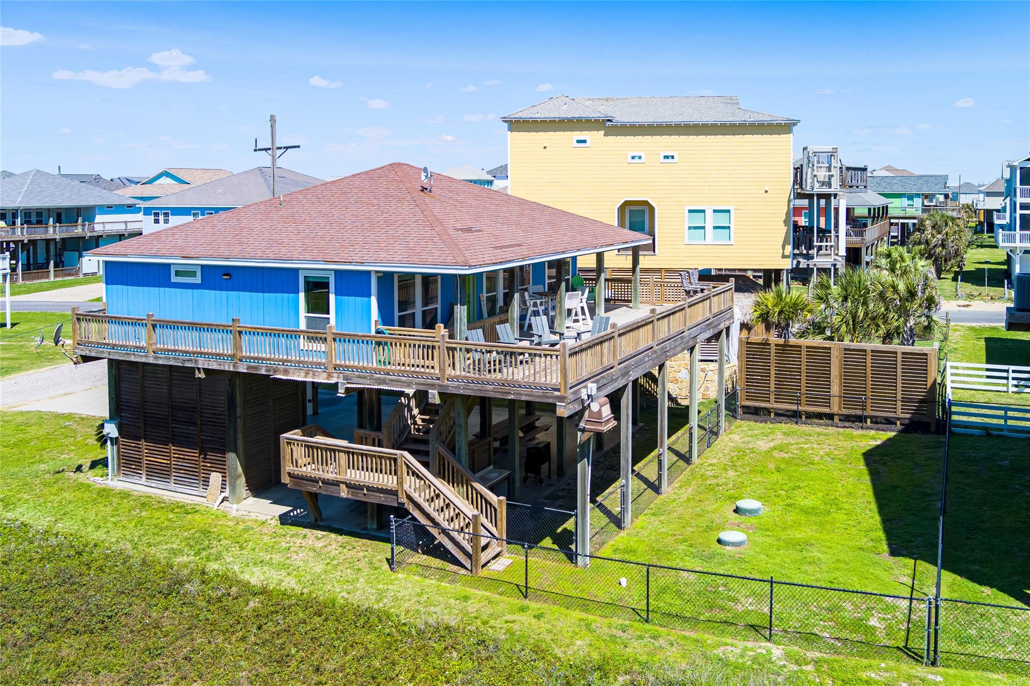 Elevated blue coastal house with a broad wooden deck and fenced yard