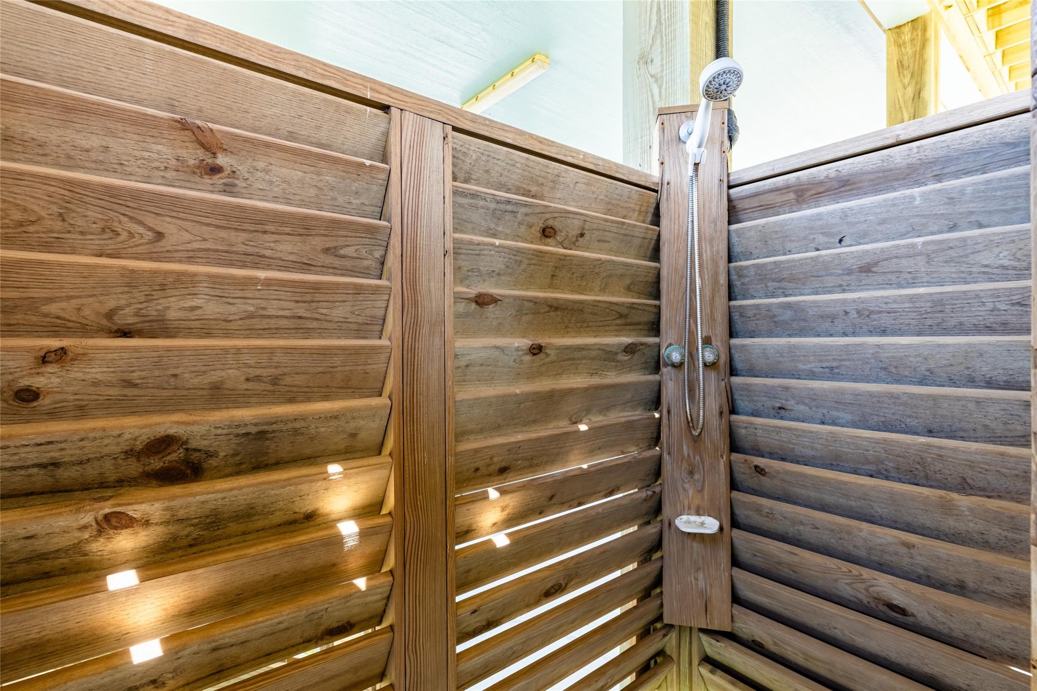 Outdoor shower with a handheld showerhead in a private wooden slat enclosure.