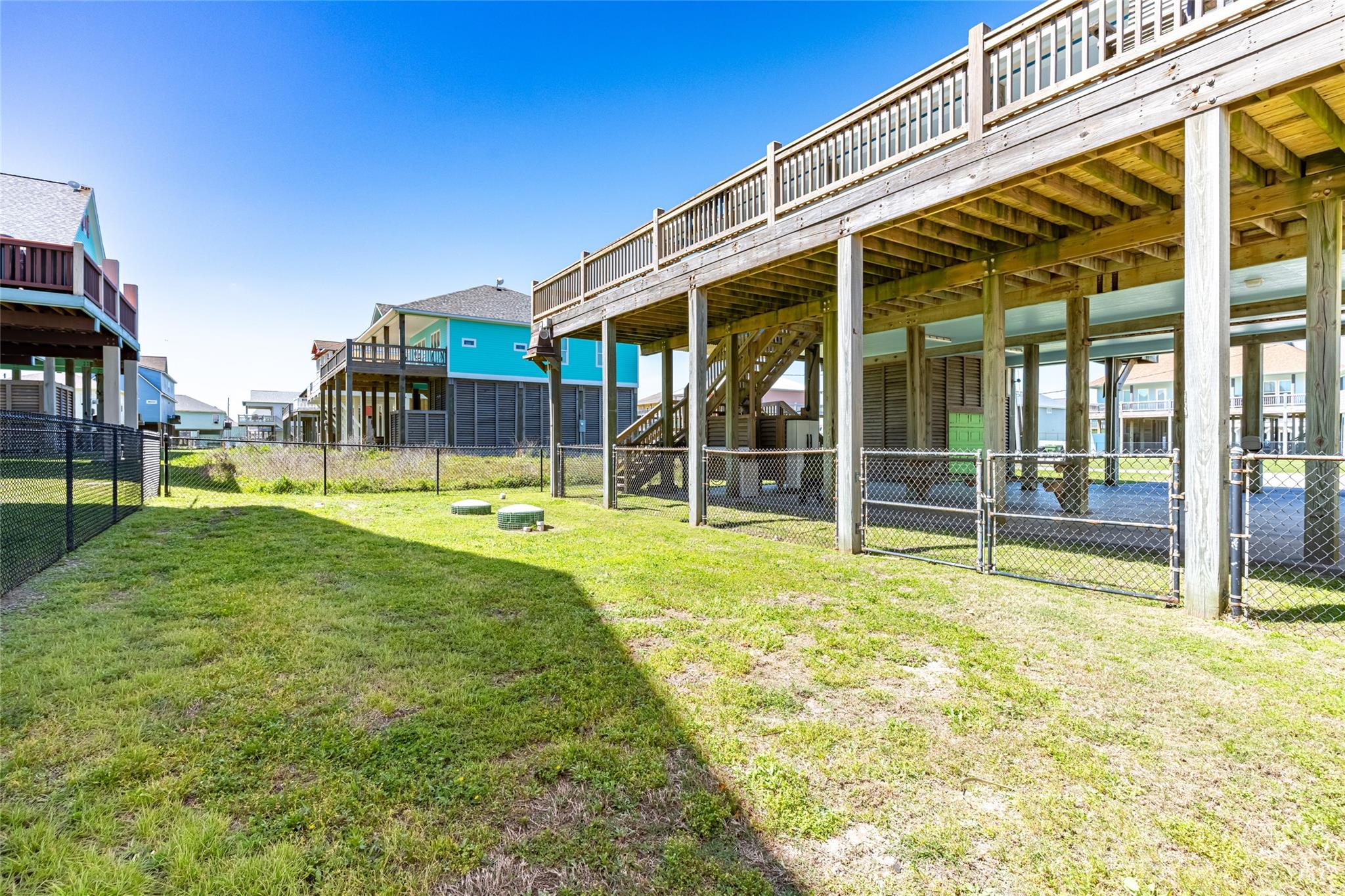 Fenced grassy backyard beneath a raised wooden deck and staircase.
