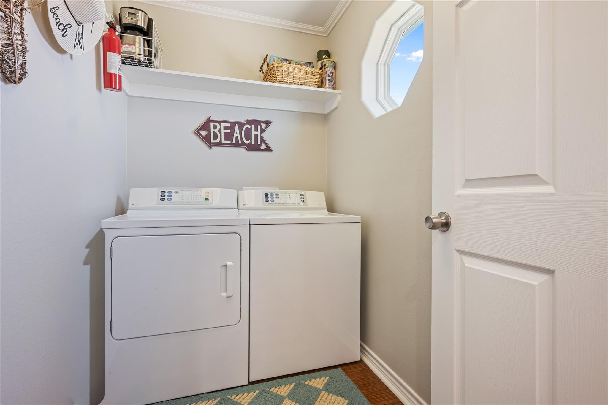 Laundry room with white washer and dryer, a BEACH sign, and an octagonal window.