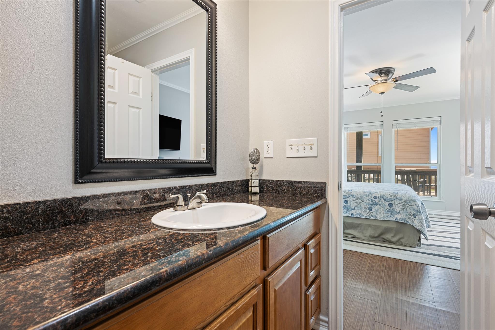Bathroom vanity with granite counter and mirror, looking through an open doorway into a bedroom.