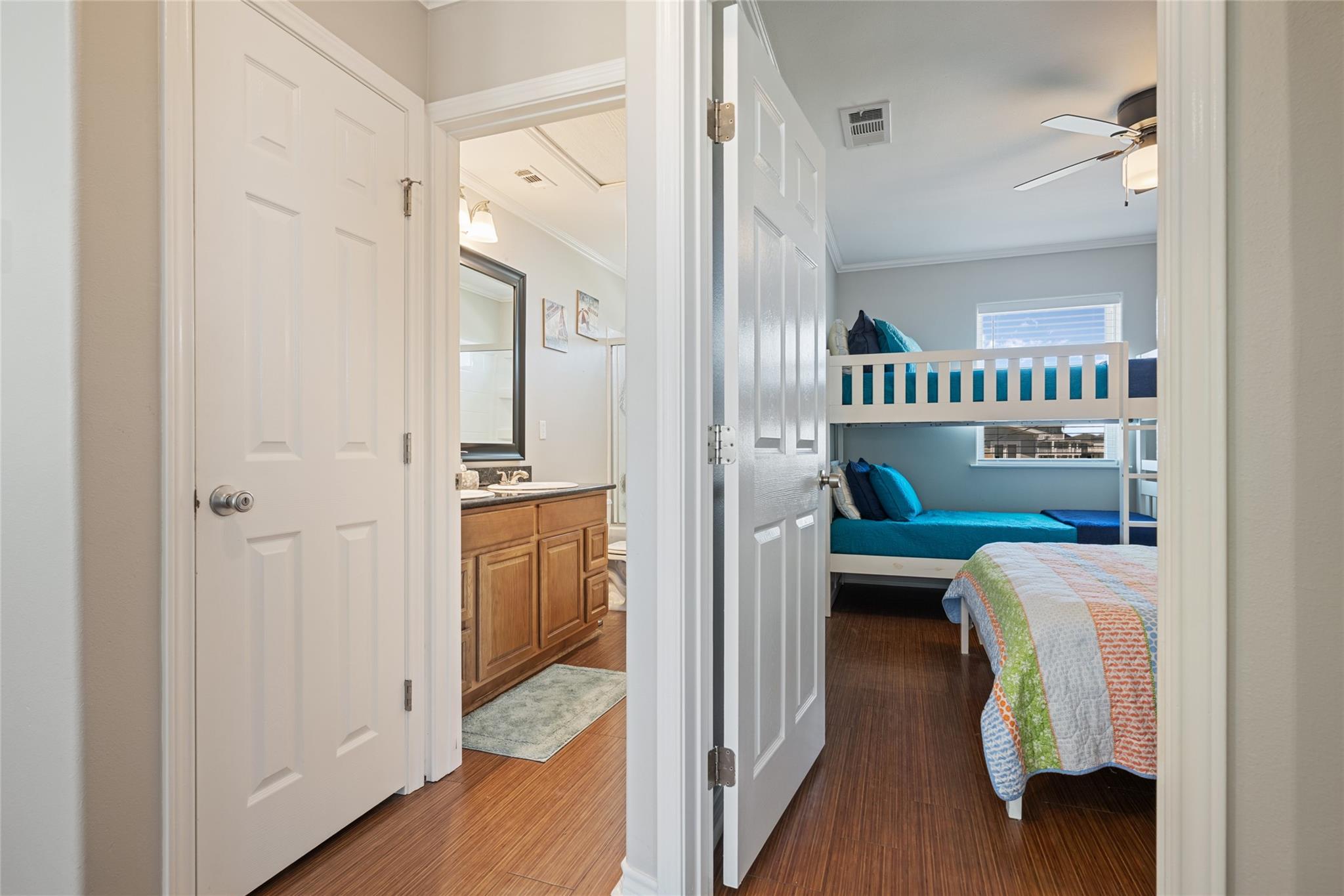 Bedroom with teal-bedded bunk beds, a colorful quilt, and an adjoining bathroom vanity.