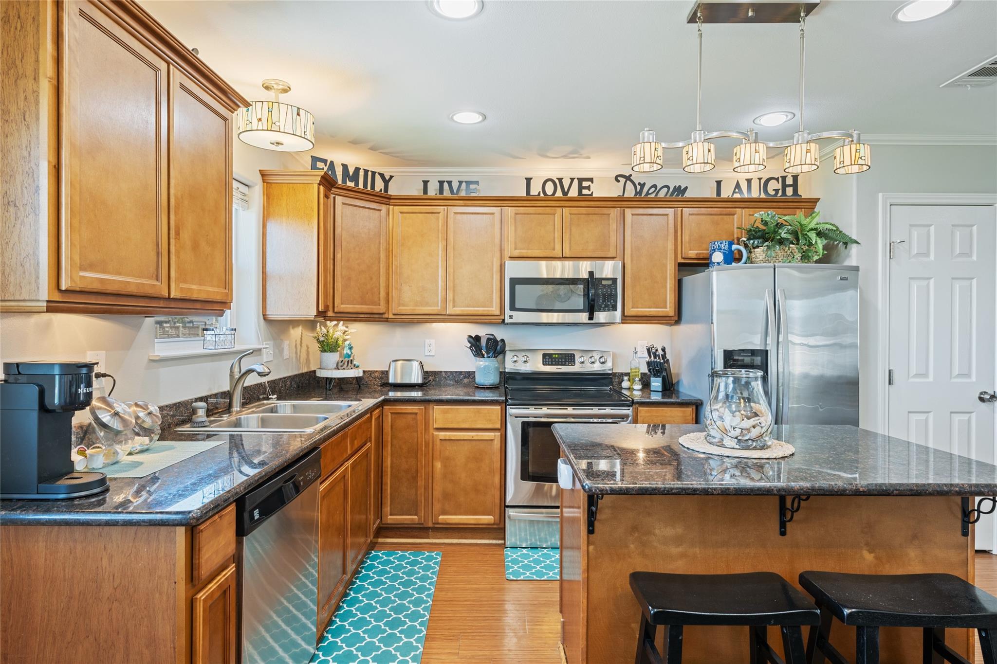 Kitchen with warm wood cabinets, stainless steel appliances, granite counters, and a large island with stools.