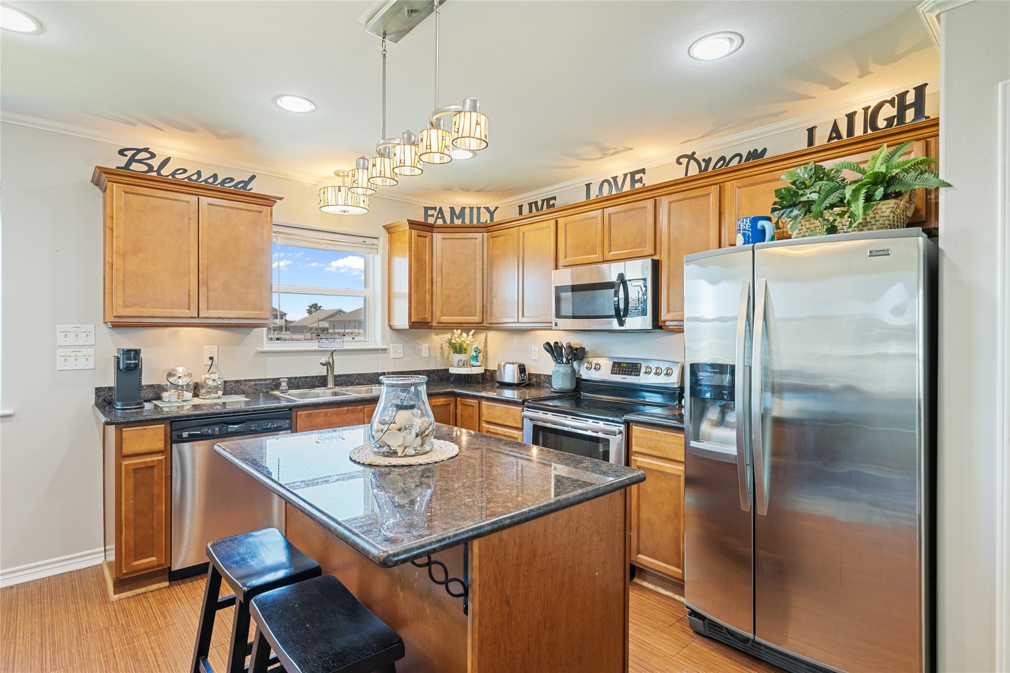 Kitchen with wood cabinets, stainless steel appliances, dark stone island, and pendant lights.