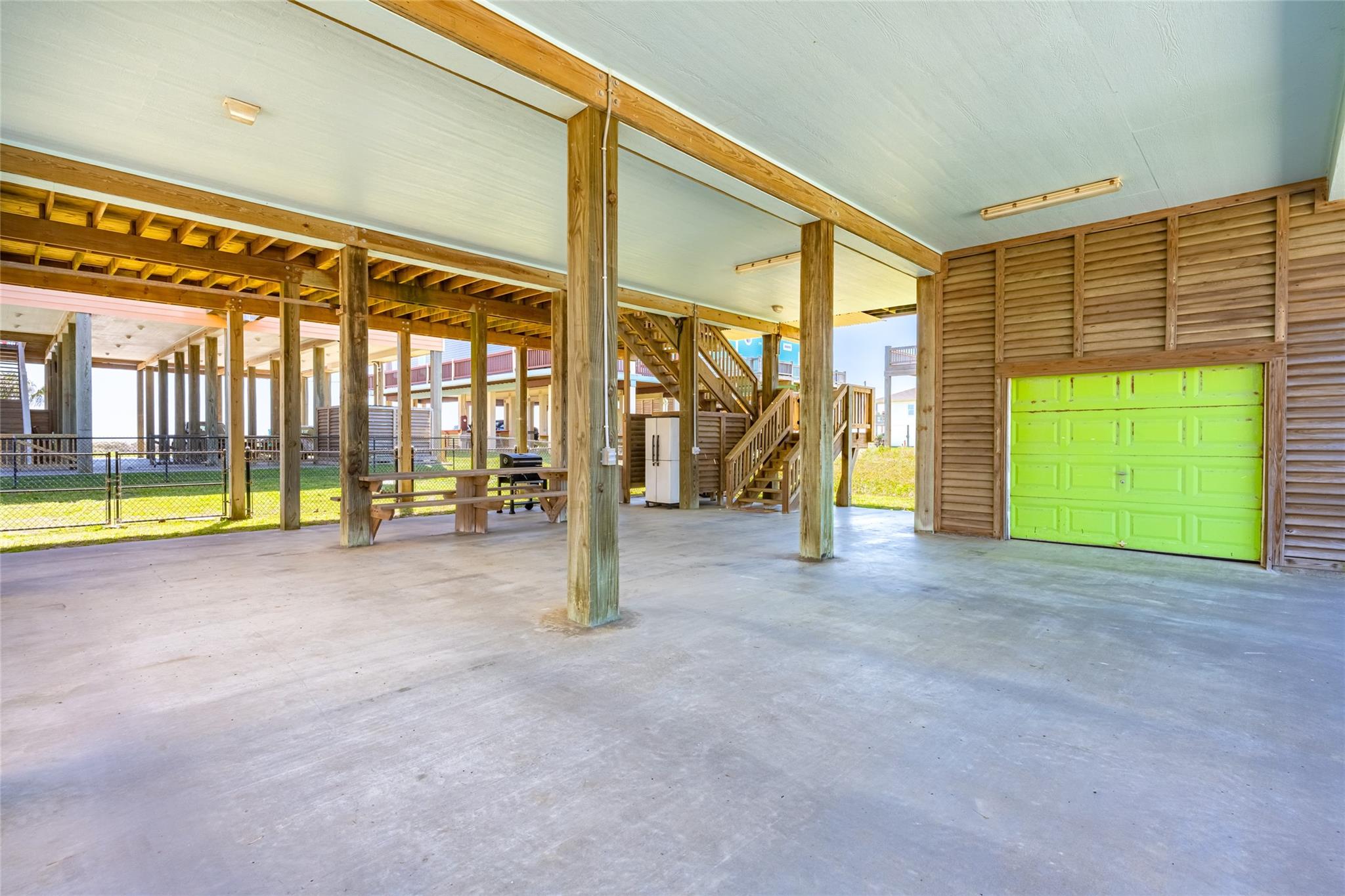 Covered area beneath a raised home with a wooden staircase, picnic table, and bright green garage door.