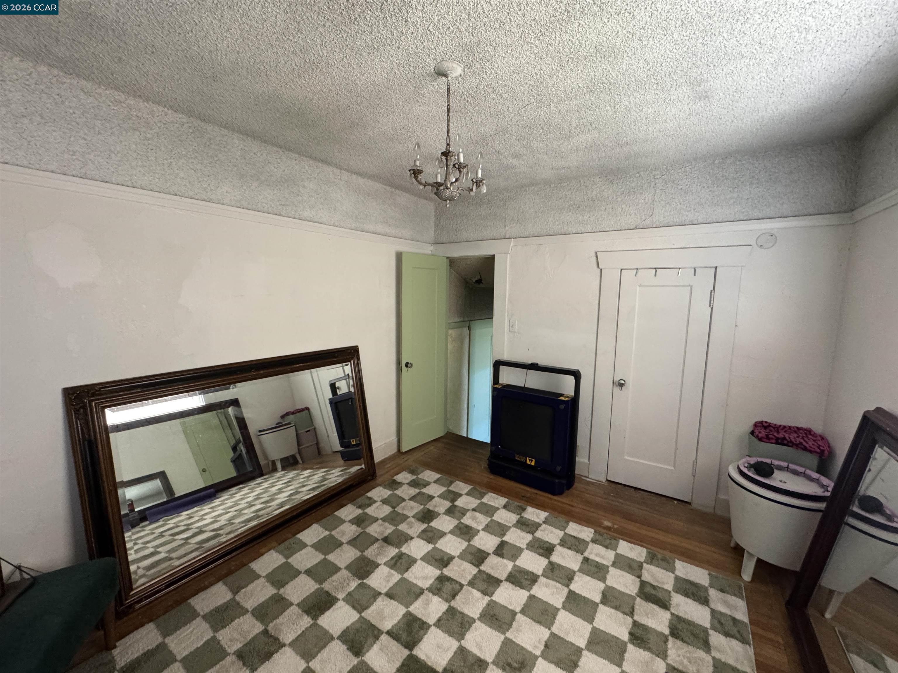 Room with a checkered rug, large leaning mirrors, chandelier, and hardwood floor.