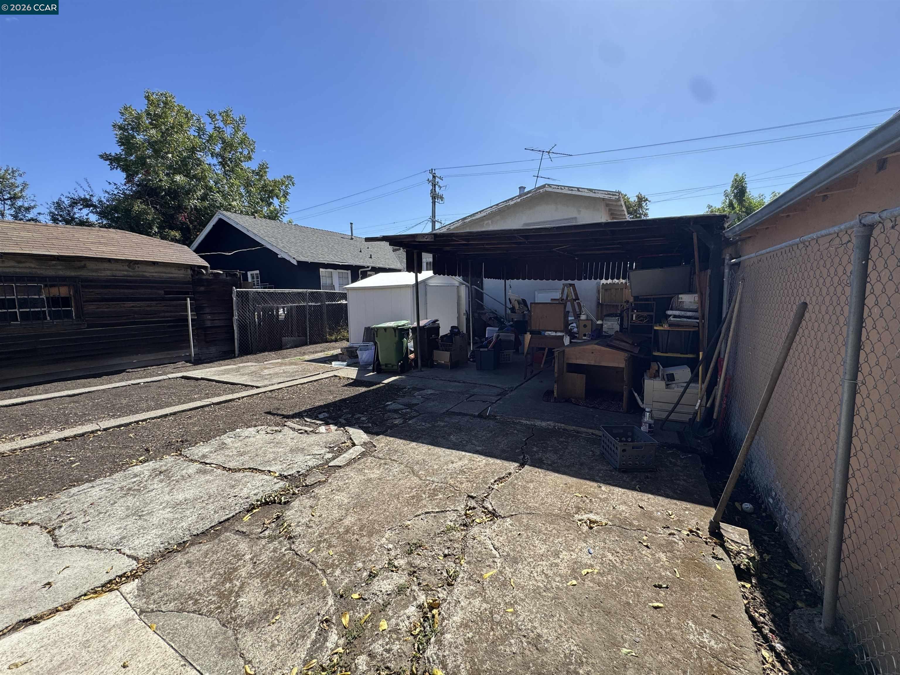 Rear yard with cracked concrete paving, a covered storage area, and chain-link fencing.