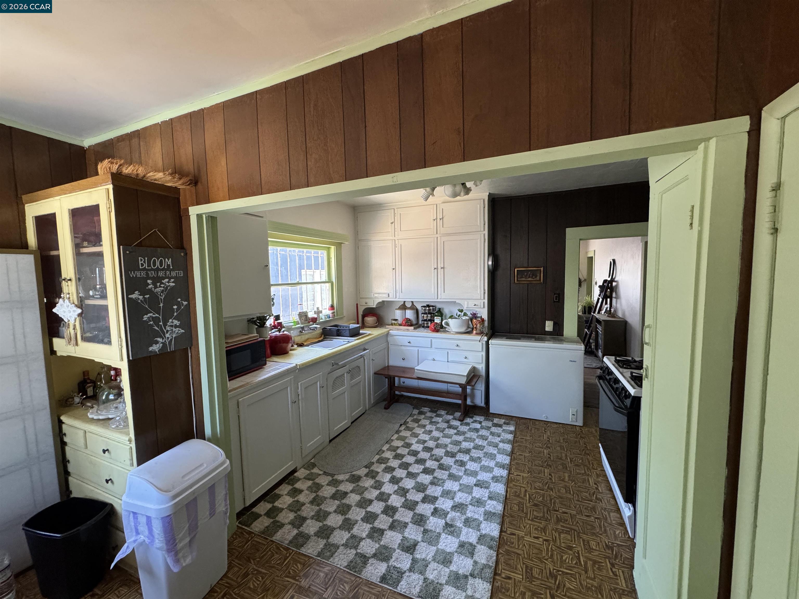 Kitchen with white cabinets, dark wood paneling, and a green-and-white checked rug.