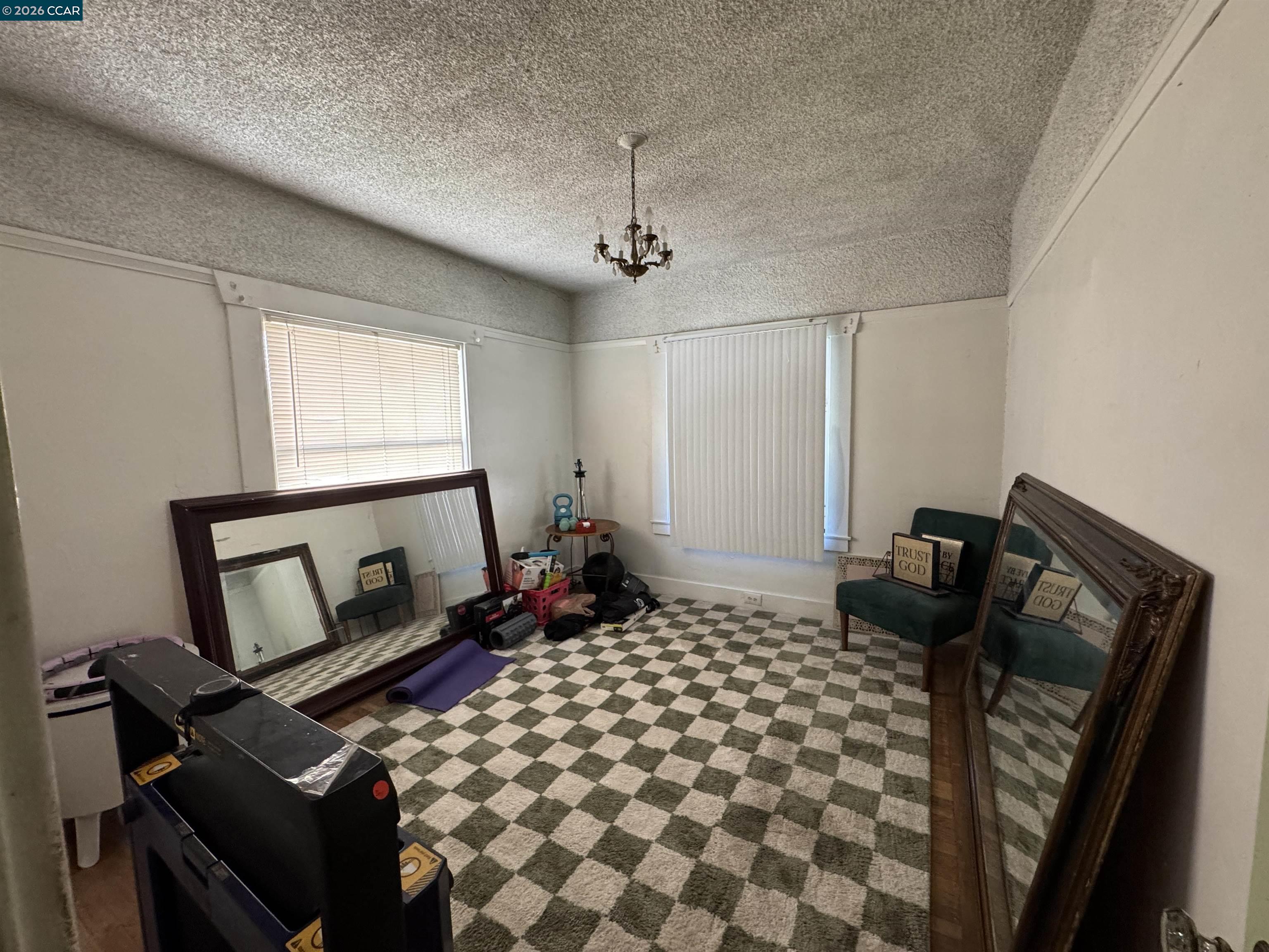 Room with checkerboard carpet, leaning mirrors, chandelier, and exercise equipment.