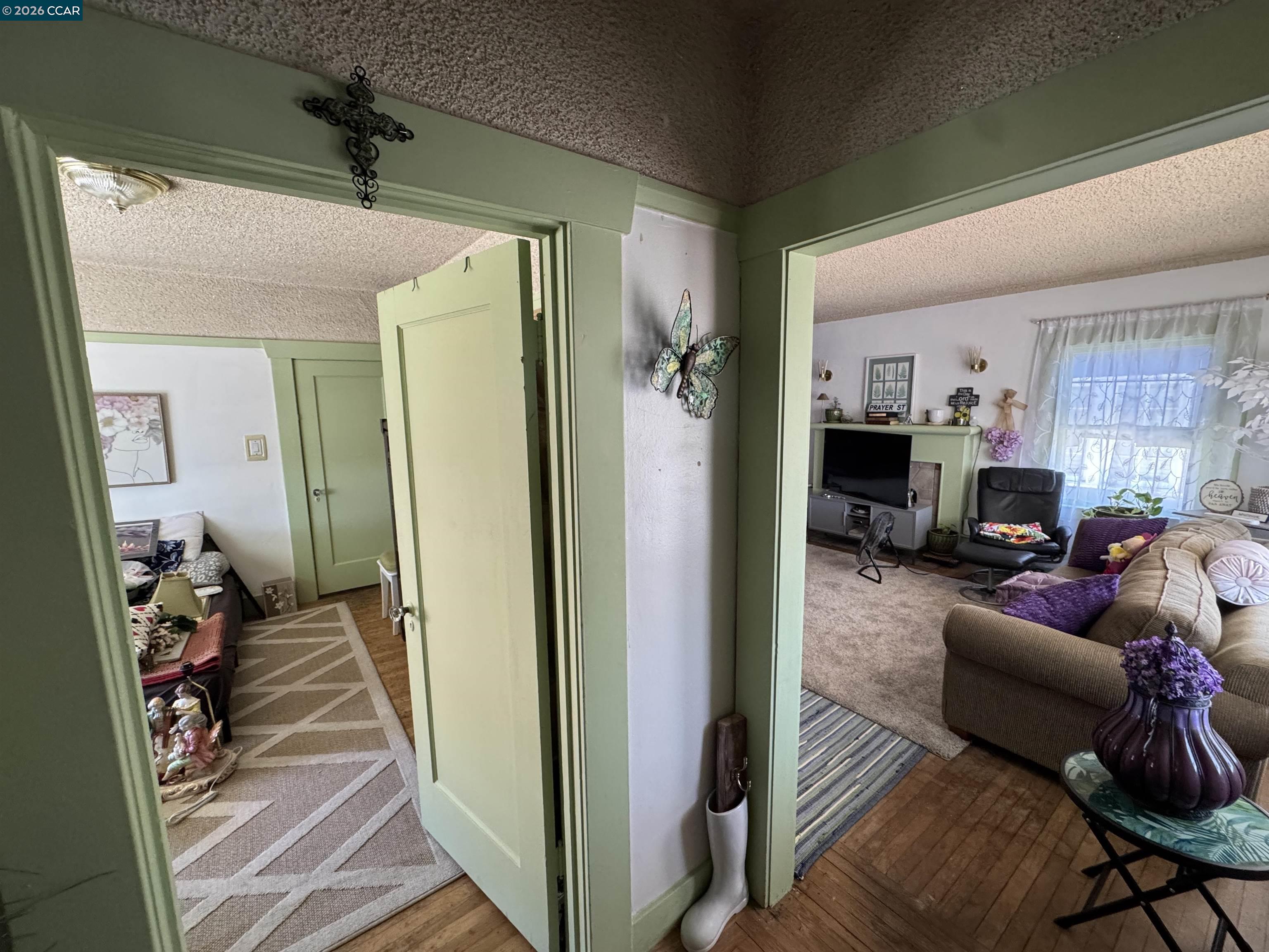 Furnished living room viewed through pale green doorways, with a fireplace, large curtained window, and hardwood floor.