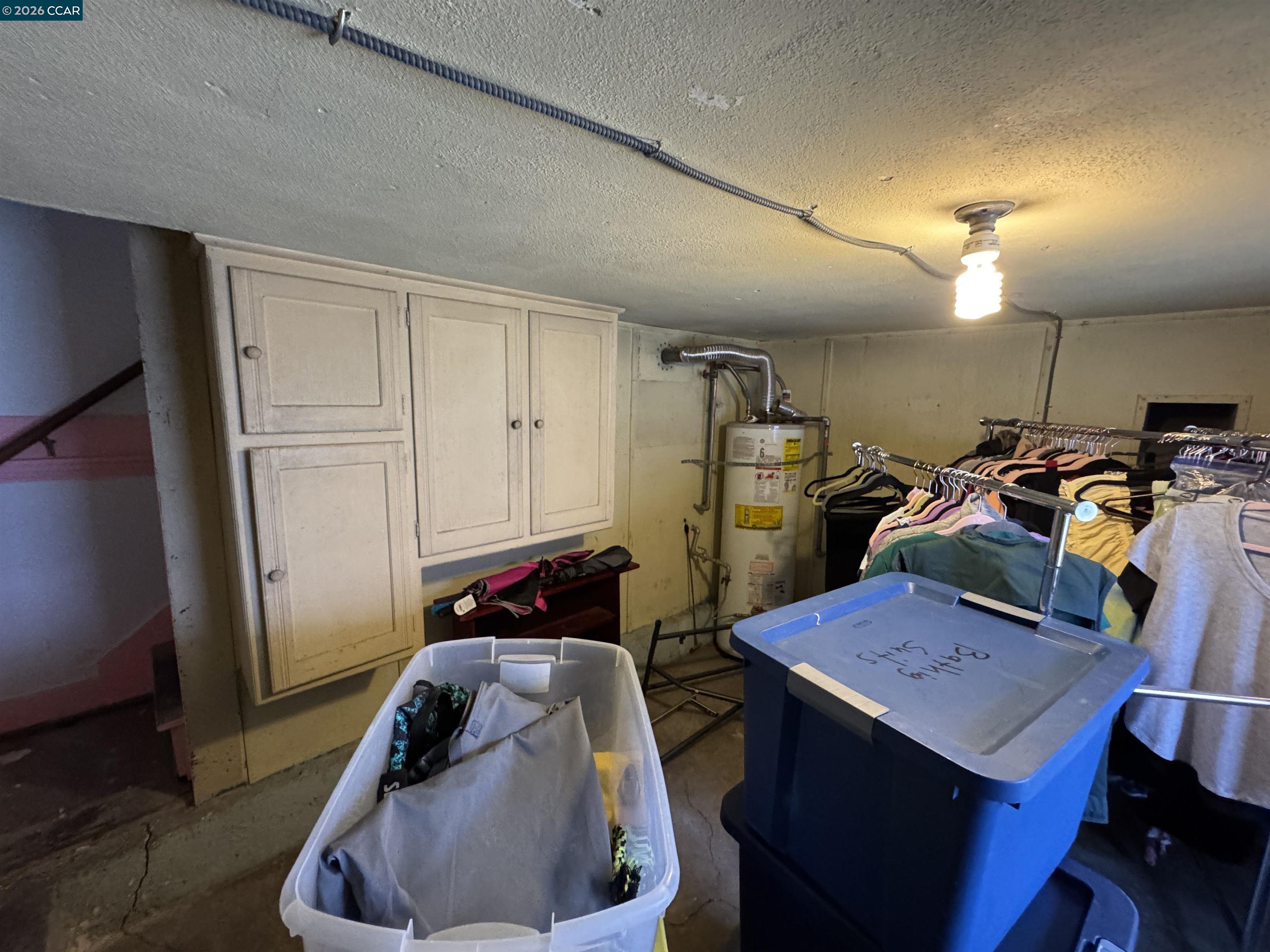 Basement utility room with built-in cabinets, a water heater, clothing racks, and storage bins.