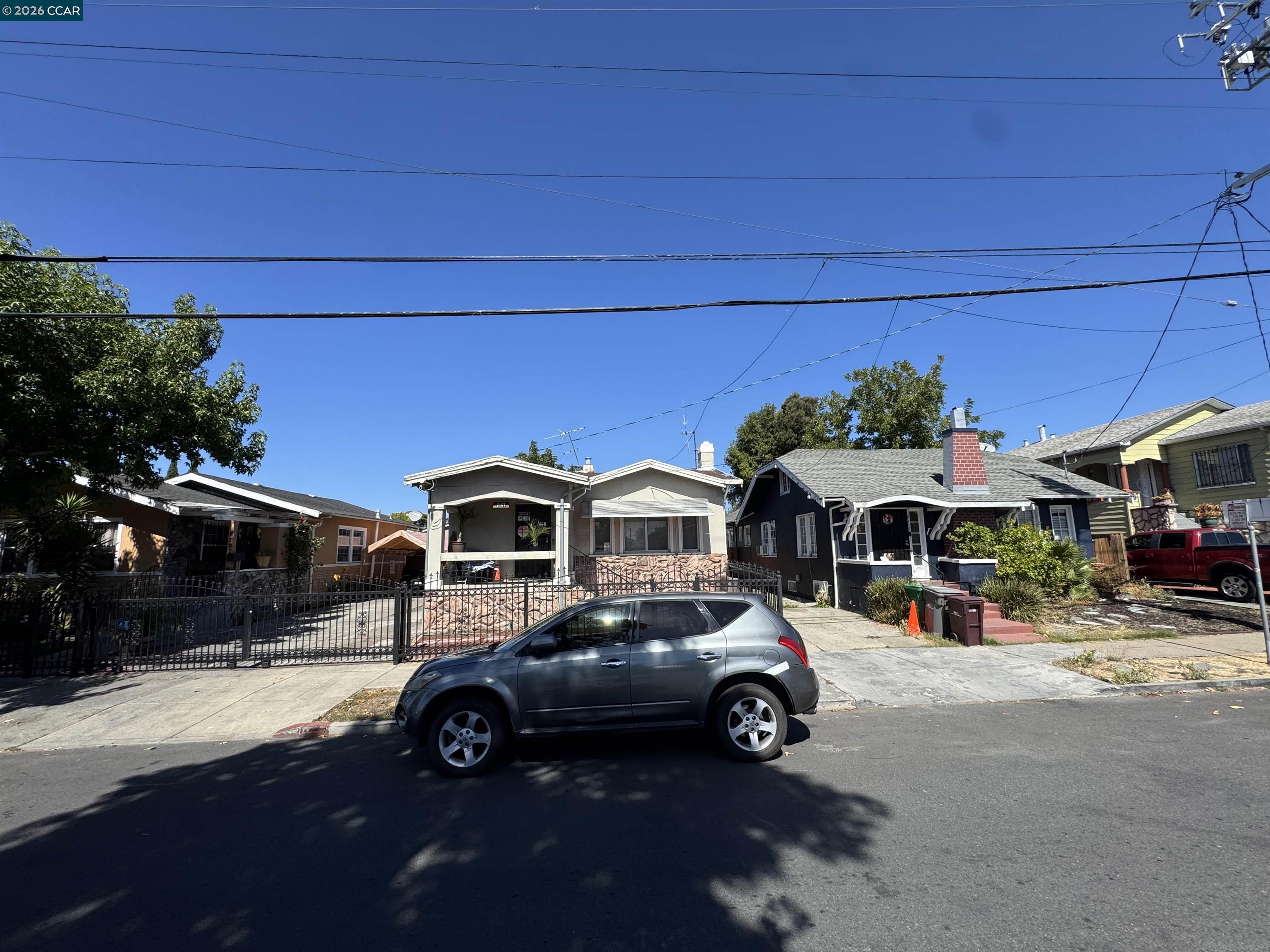 Gray bungalow with a stone facade, covered porch, and black iron fence along an Oakland street.