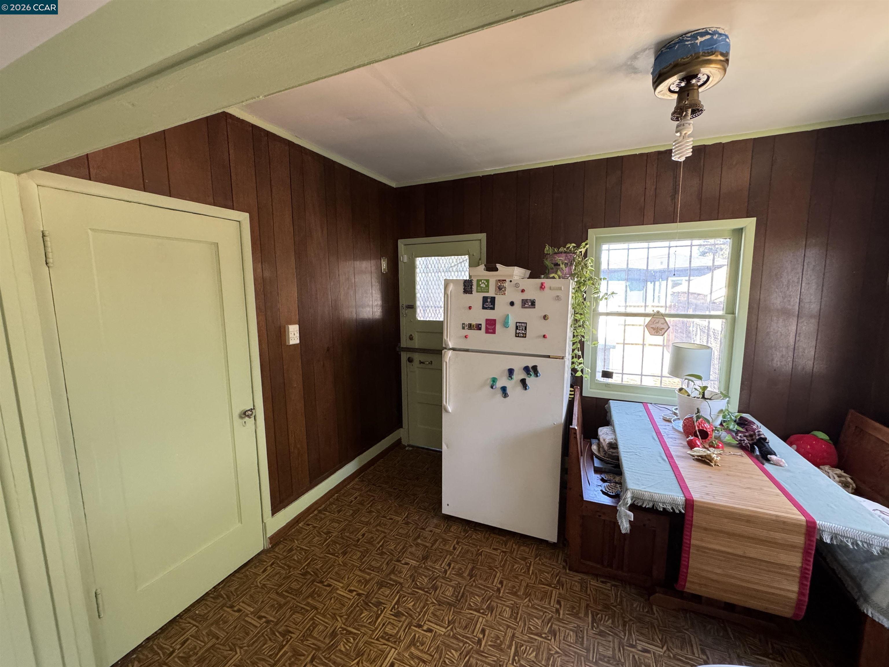 Kitchen and dining area with dark wood-paneled walls, pale green trim, and a refrigerator beside the table.