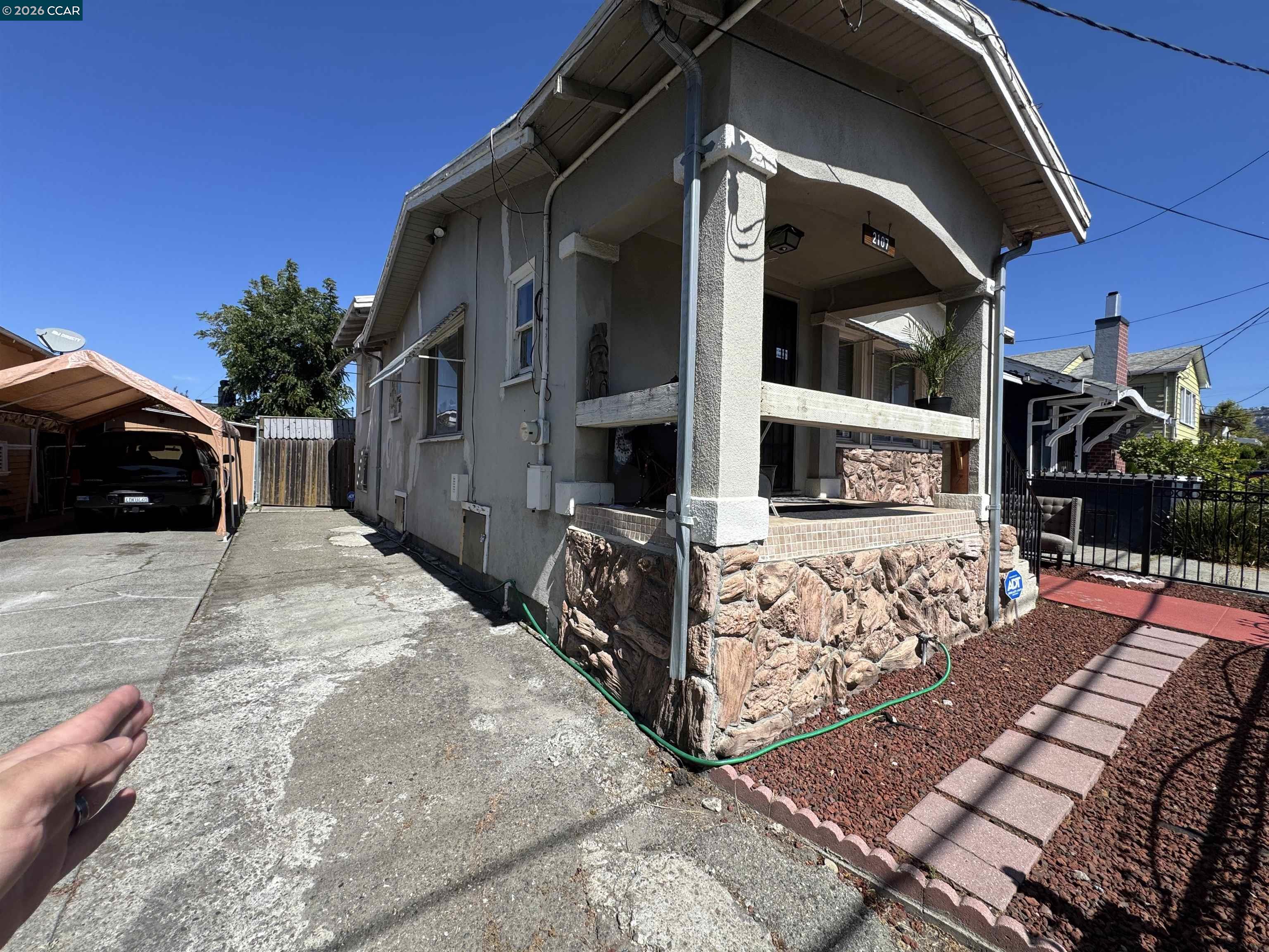 Gray house with a covered porch, stone foundation, and driveway beside a carport.