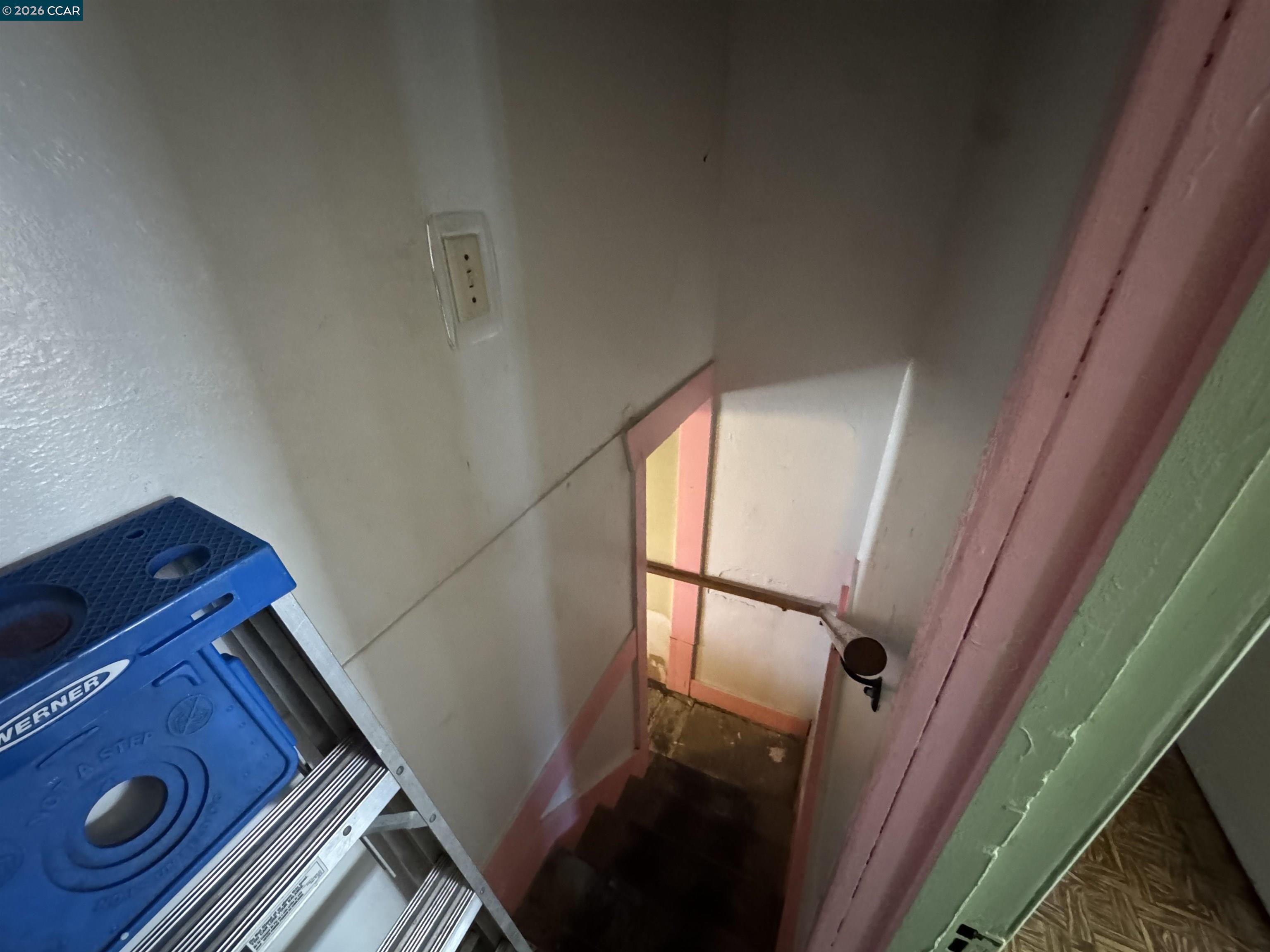 Narrow staircase with pink trim and a blue step ladder at the top.