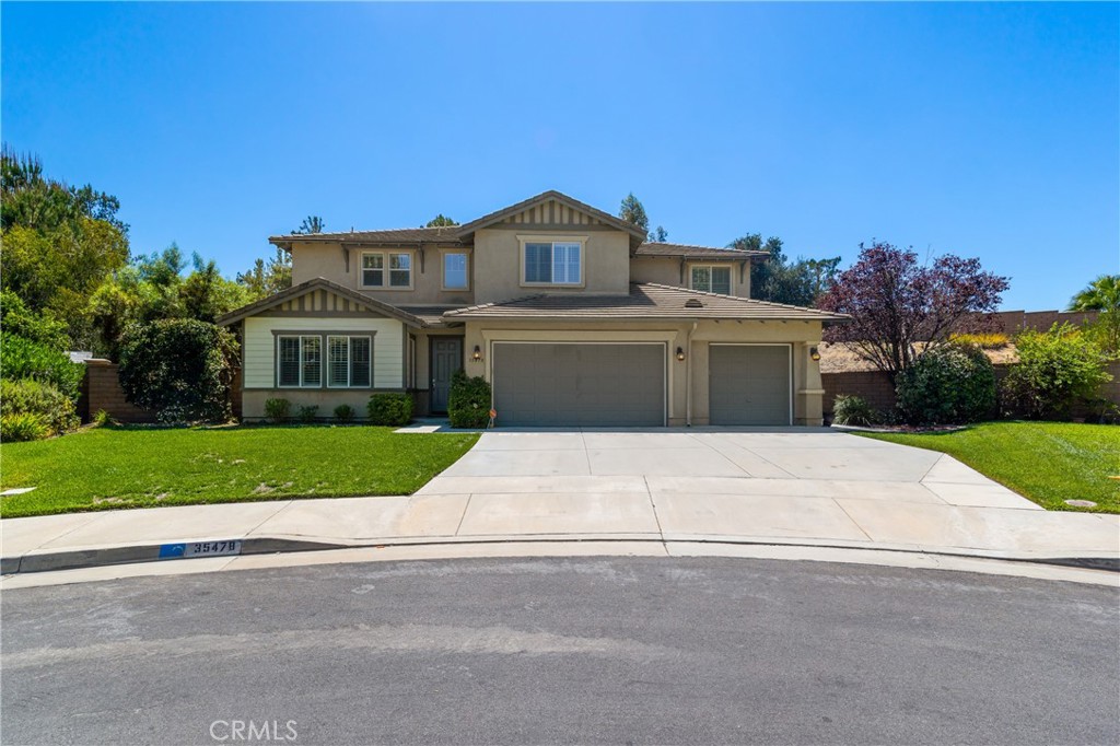Two-story stucco house with a wide driveway, two garage doors, and landscaped lawn.