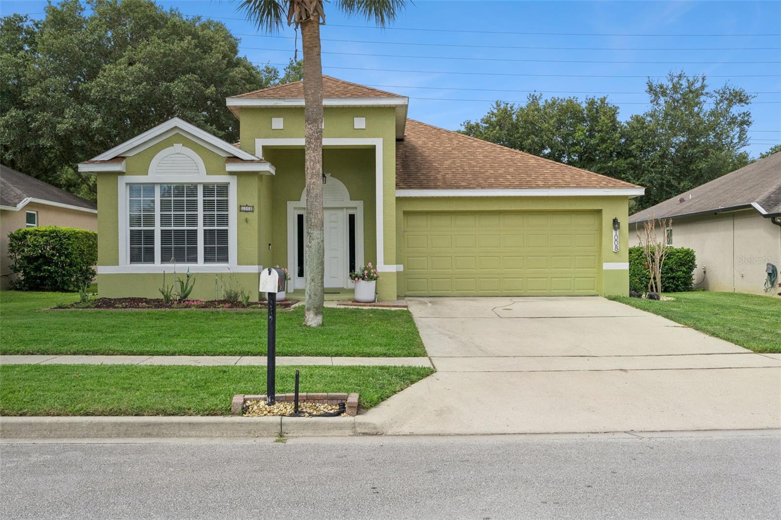 Pale green Florida home with white trim, a two-car garage, and a palm tree in front.