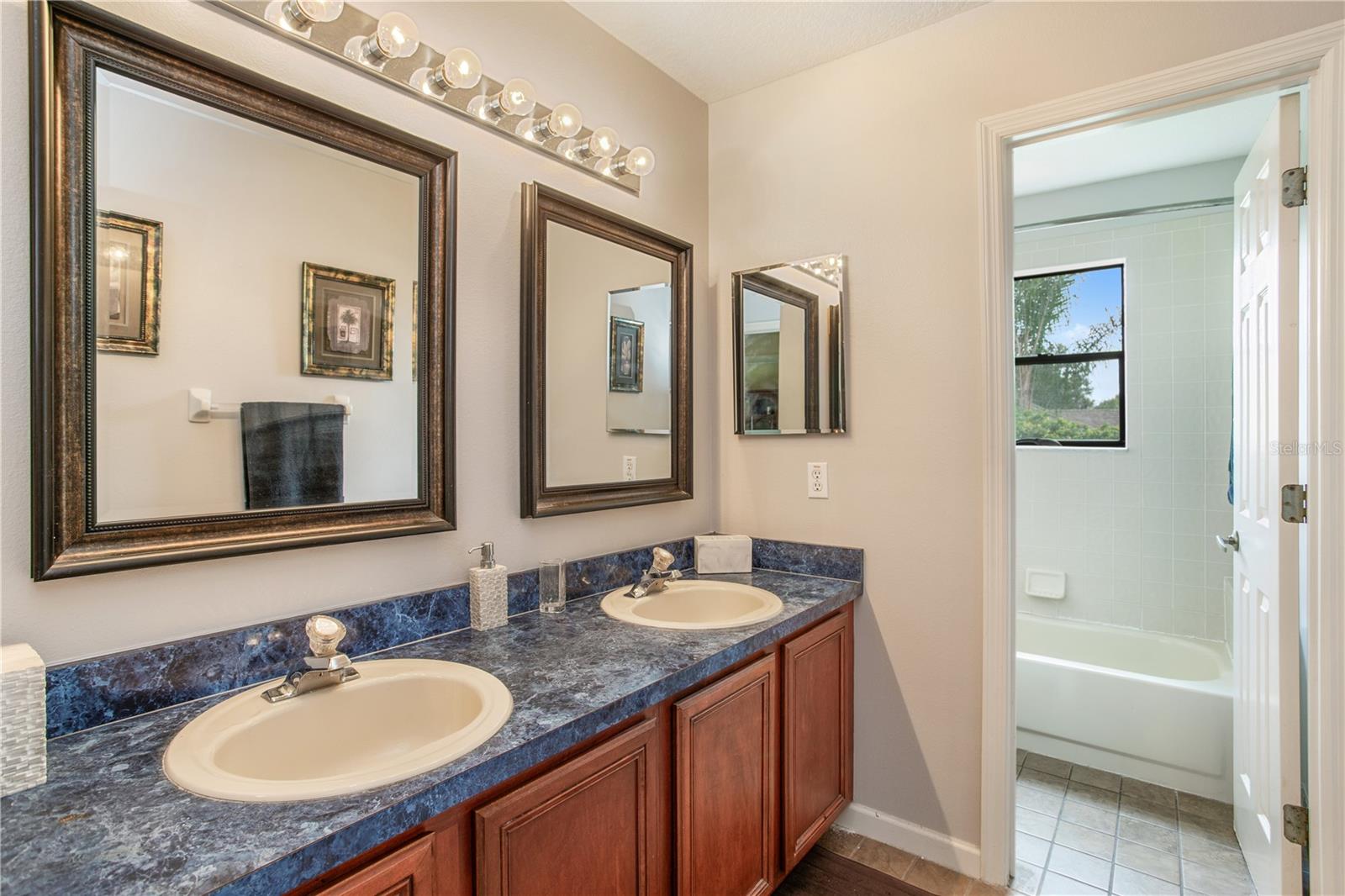 Bathroom with double-sink vanity and blue marbled countertop; tiled tub and shower visible through doorway.
