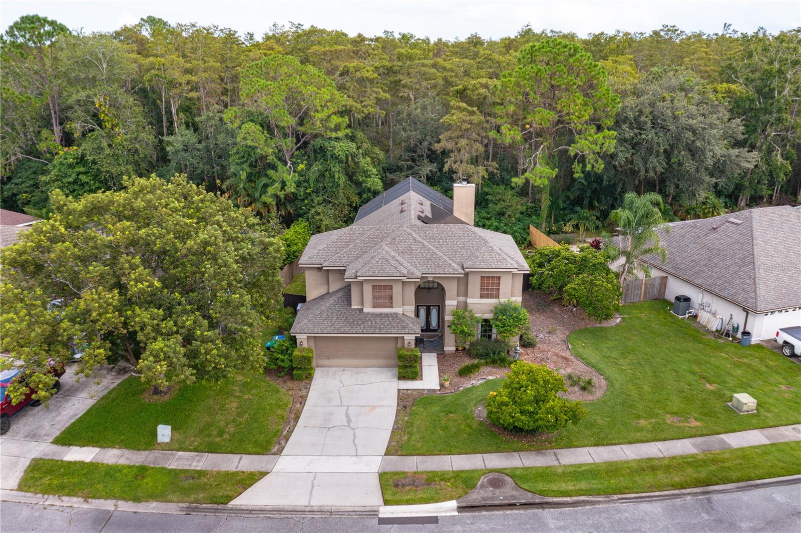 Two-story beige home with a front-entry garage, concrete driveway, and dense trees behind it.