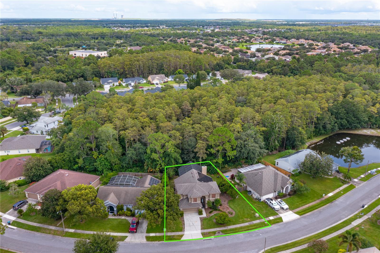 Aerial view of a home outlined in green beside a wooded area and pond.