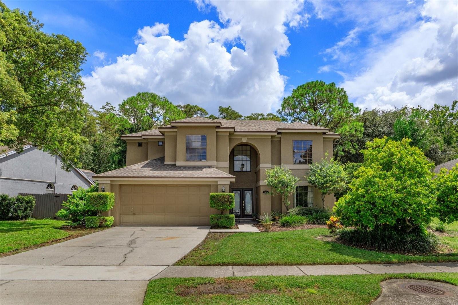 Two-story tan stucco home with an arched entry, double garage, and landscaped front yard.