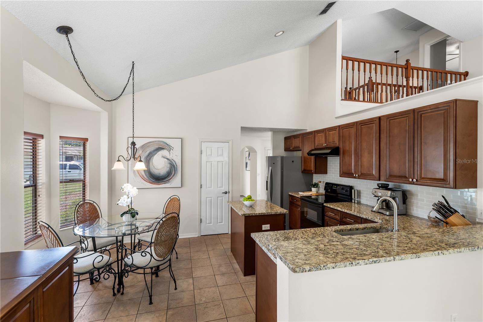 Open kitchen and dining area with granite counters, dark wood cabinets, and an upstairs balcony railing.