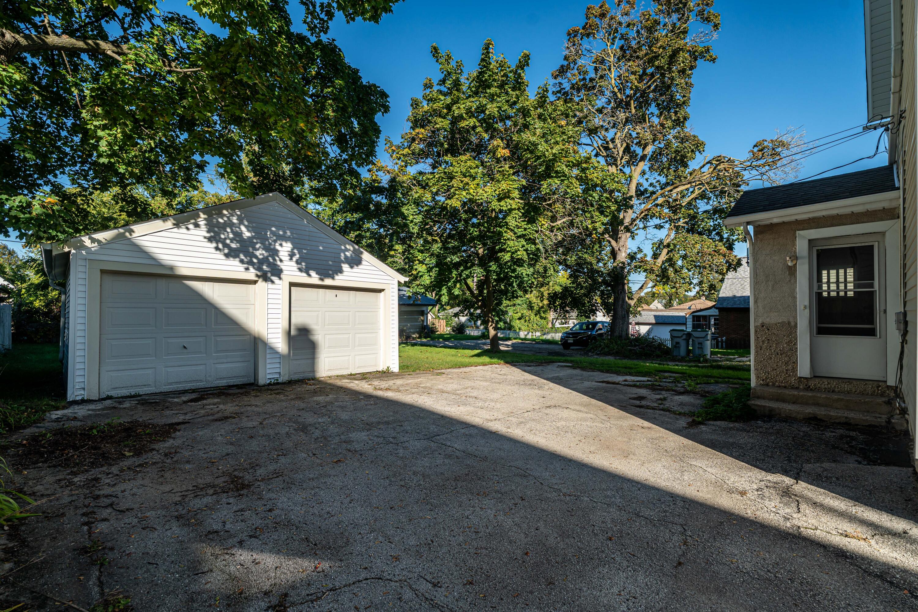 Detached two-car garage beside a broad paved driveway, shaded by mature trees.