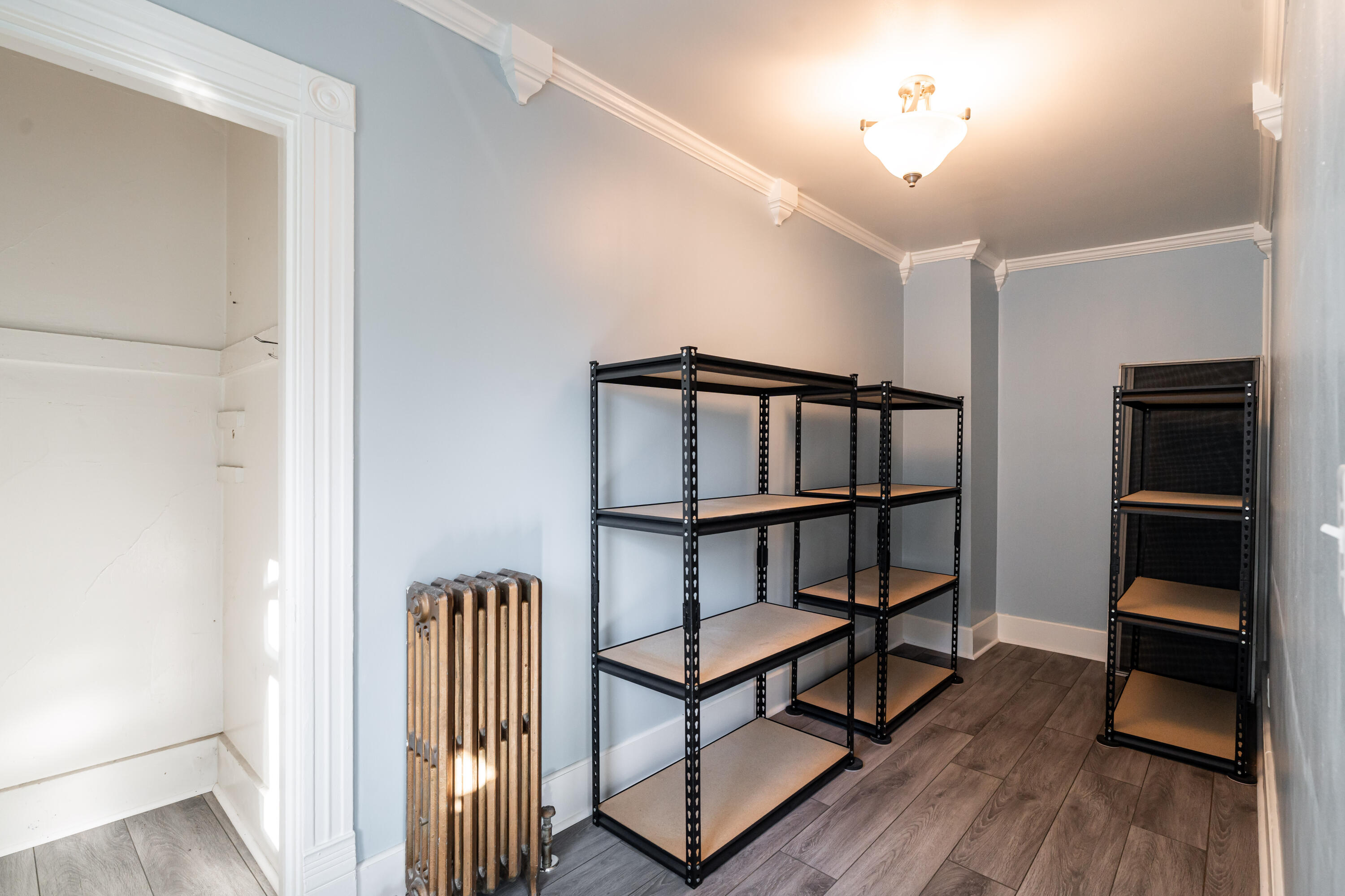 Storage room with black metal shelving, a cast-iron radiator, and decorative crown molding.