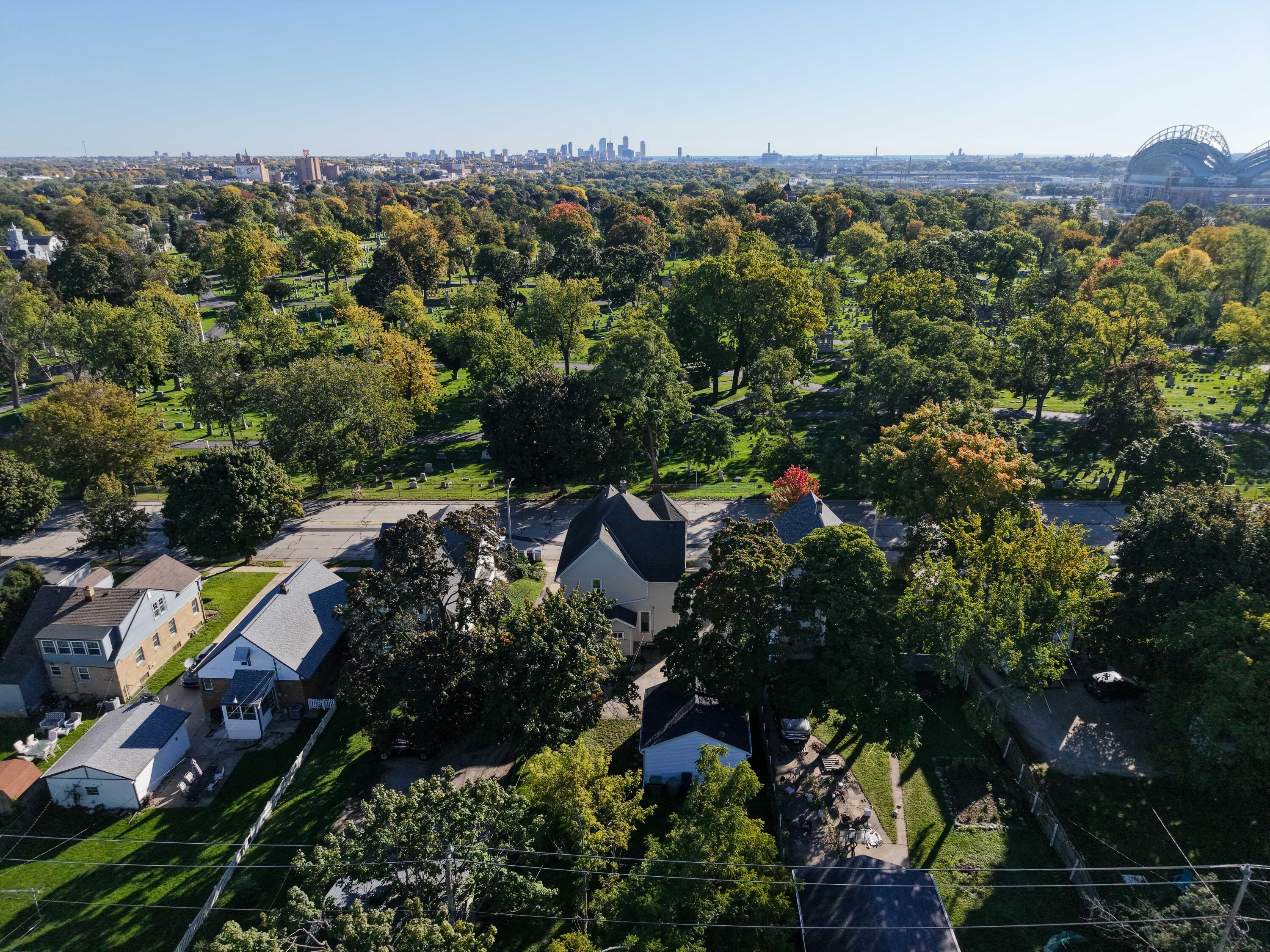 Aerial view of homes beside a tree-filled cemetery, with the Milwaukee skyline in the distance.