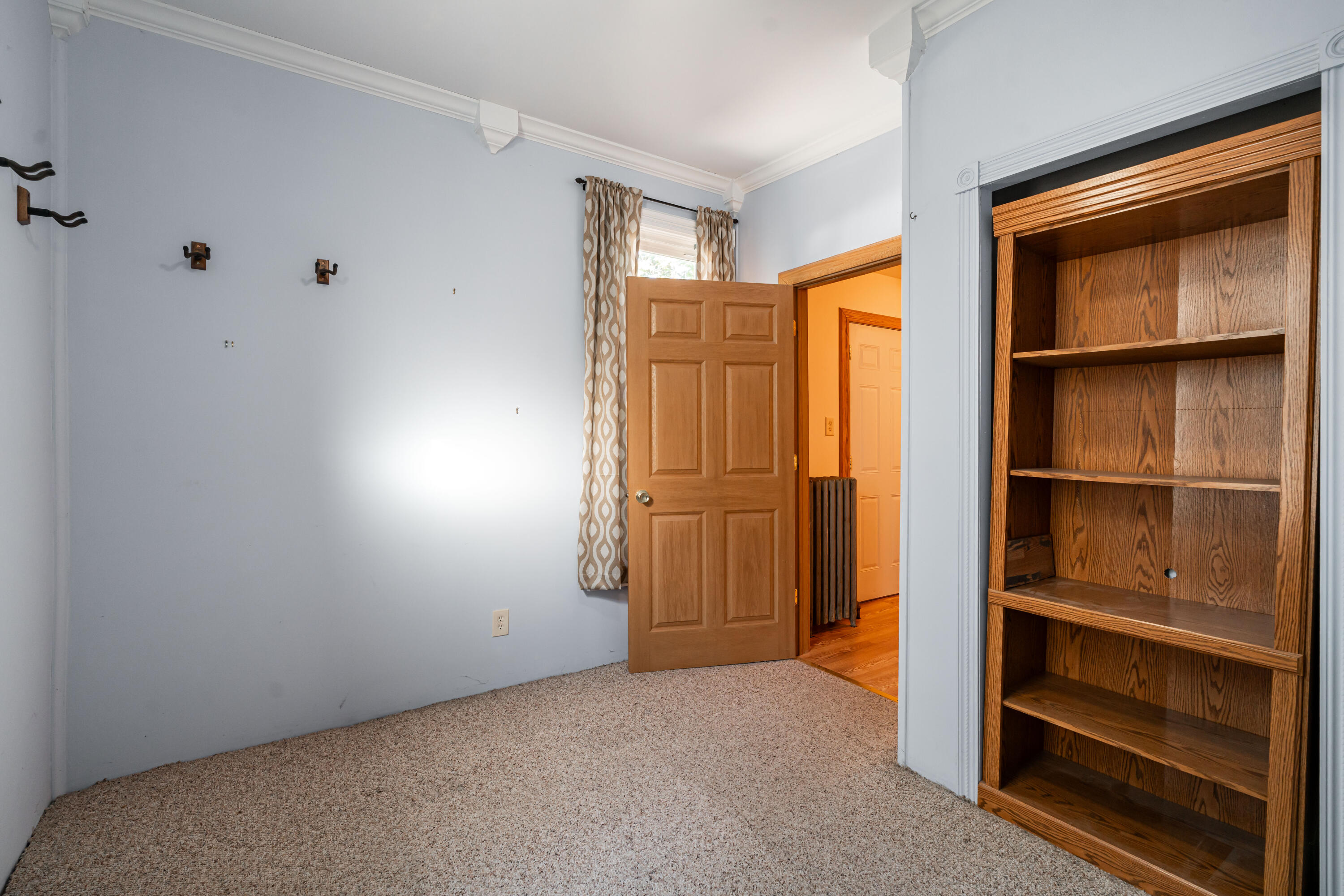 Empty carpeted bedroom with a built-in oak bookcase and open wooden door.