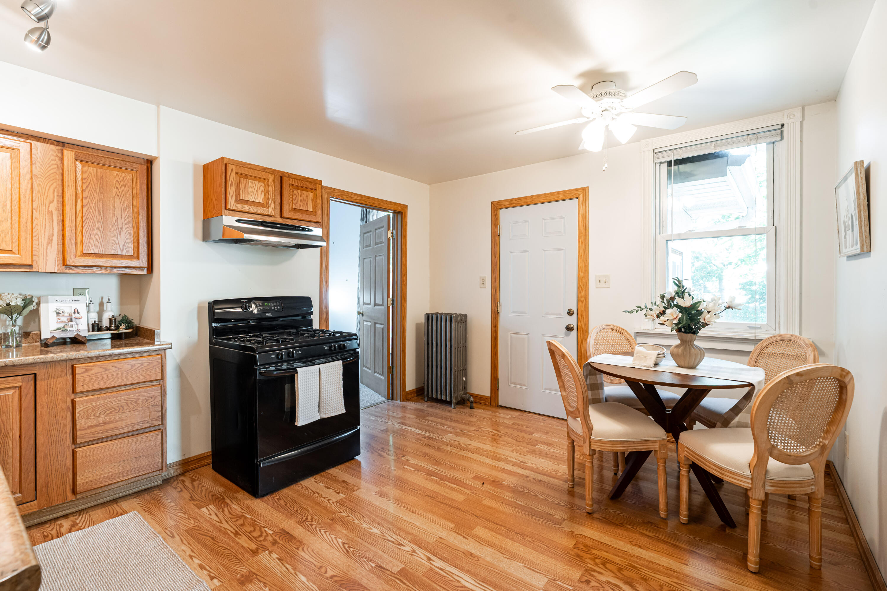 Kitchen and dining area with oak cabinetry, hardwood floors, and a round table beside a large window.