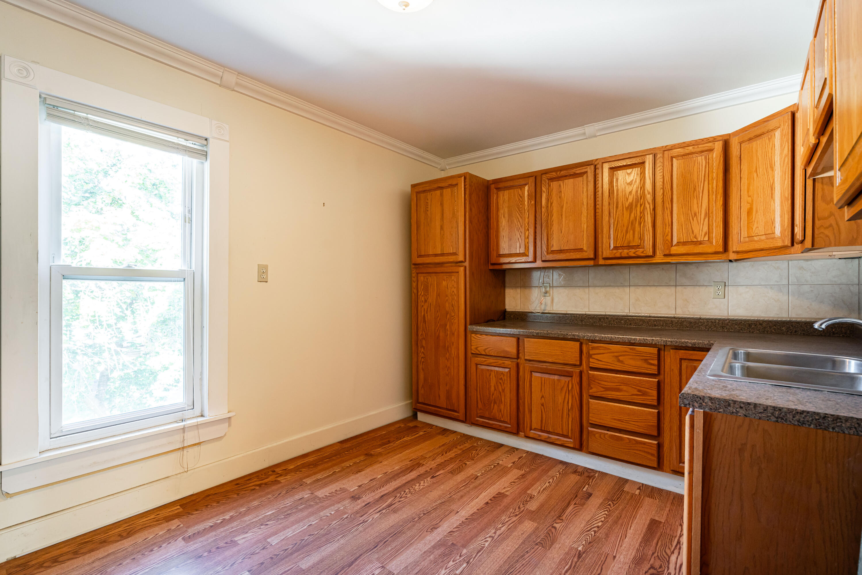 Kitchen with oak cabinets, hardwood floors, tiled backsplash, and a large window.