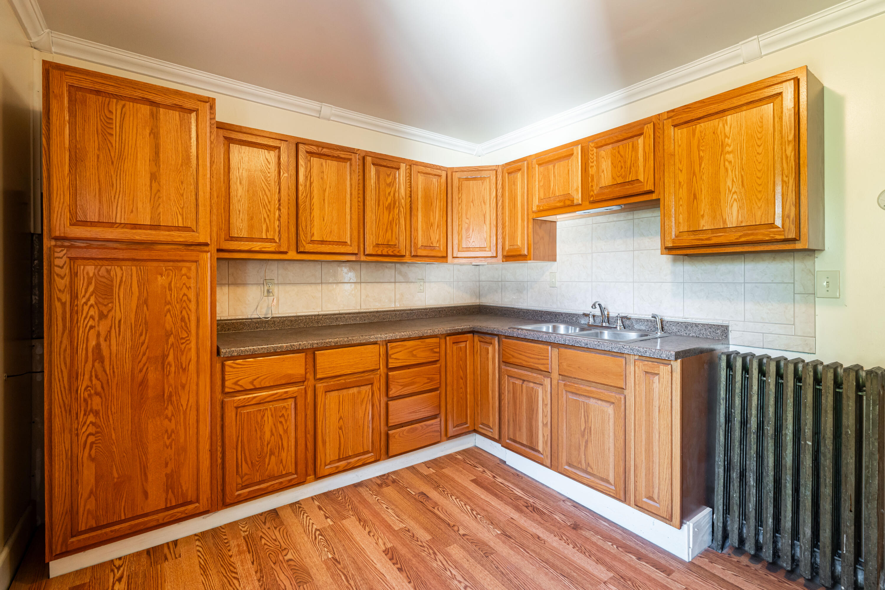 Kitchen with honey-colored wood cabinets, tiled backsplash, double-basin sink, and hardwood floors.