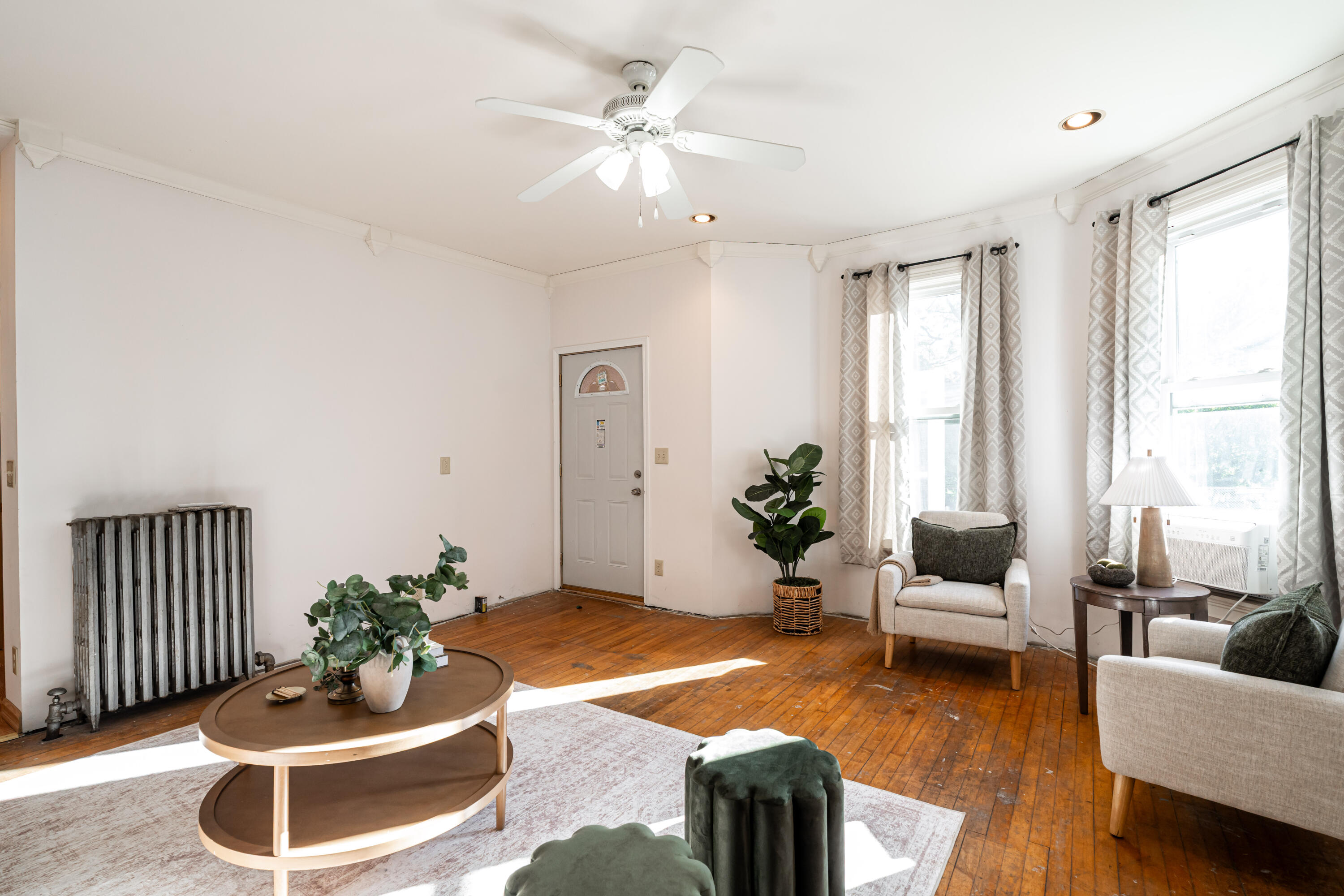 Furnished living room with hardwood floors, large windows, and a vintage radiator.