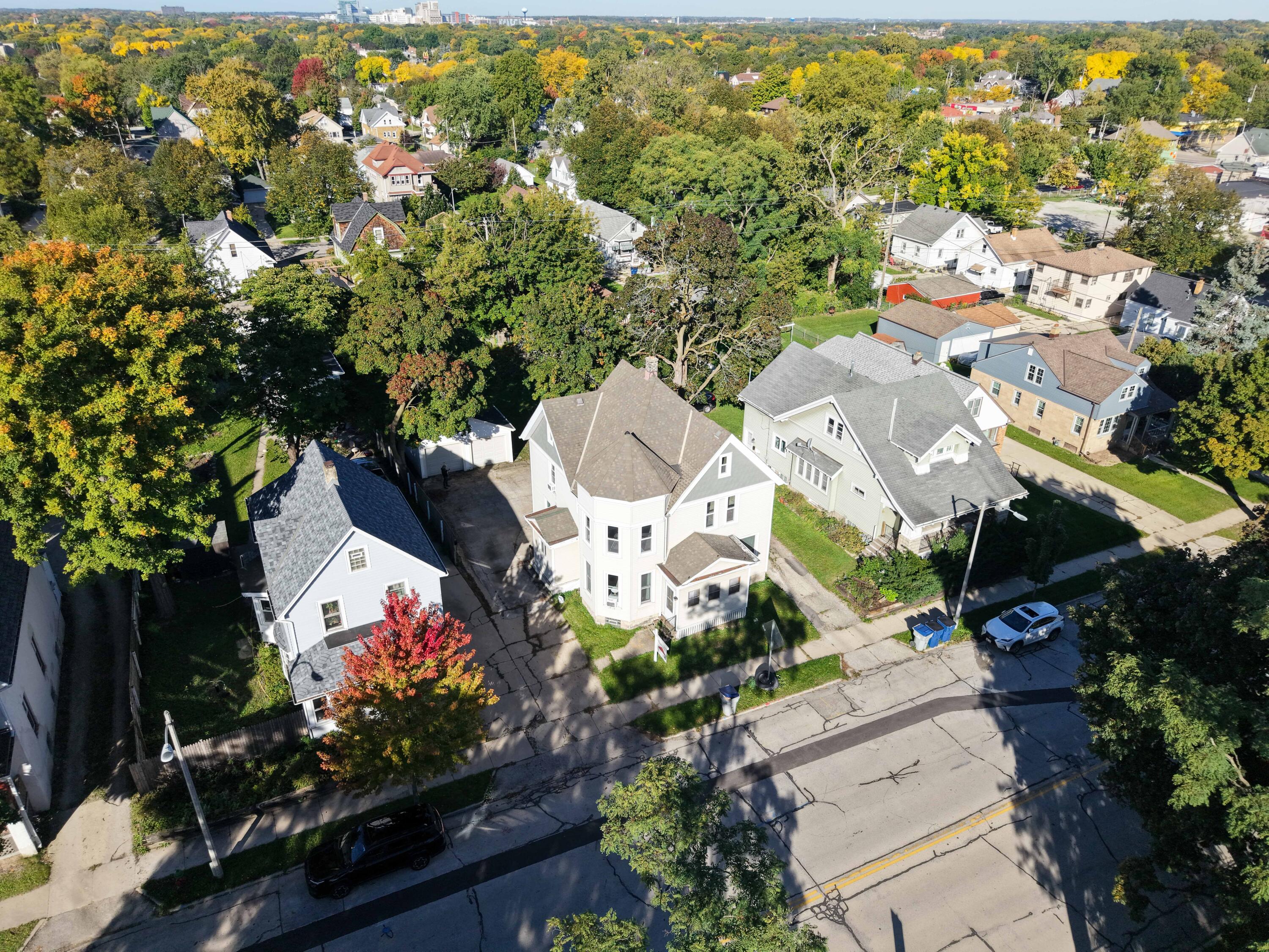 Aerial view of a white multi-story house with a projecting bay window amid tree-lined residential streets.