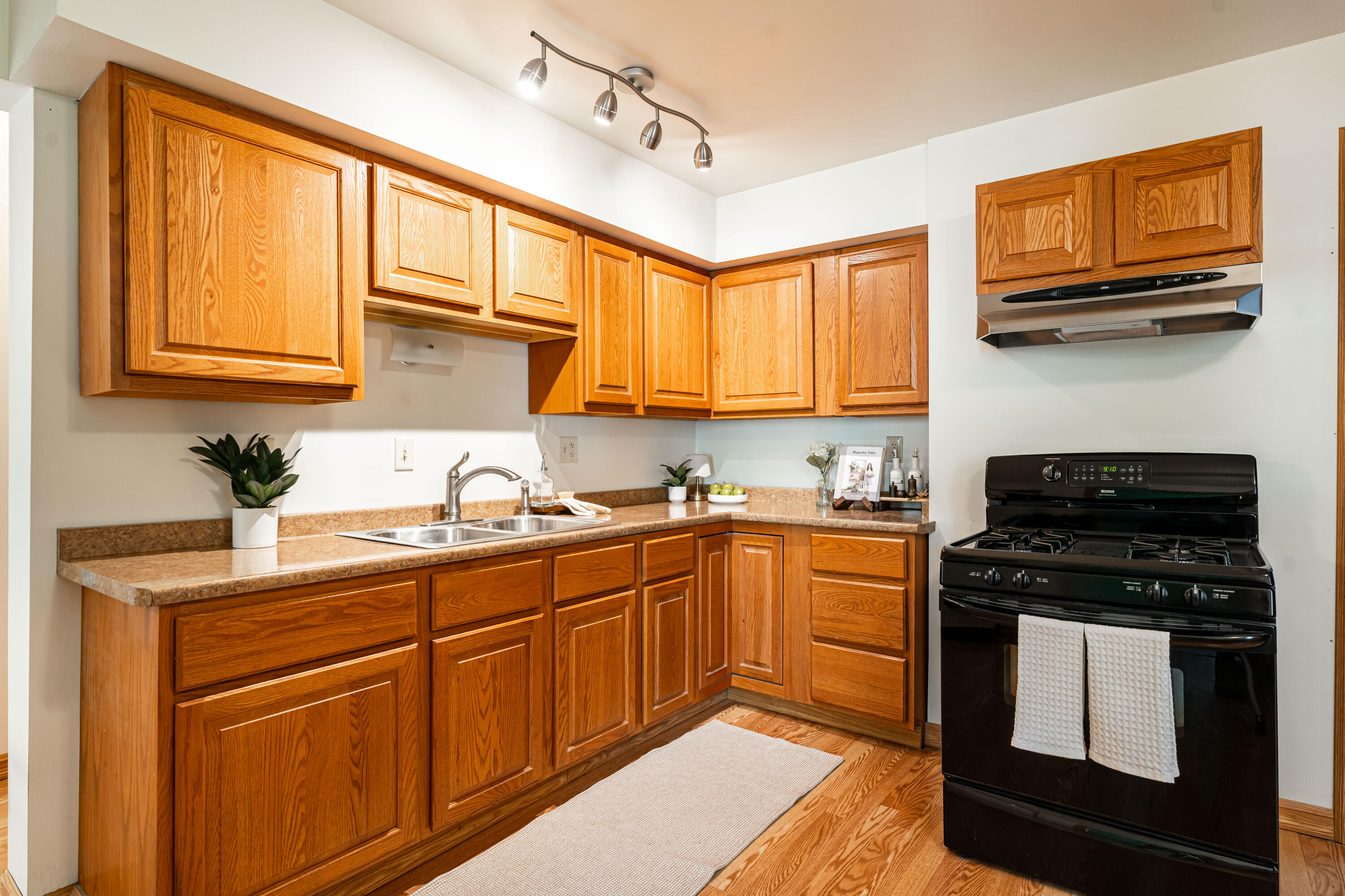 Kitchen with warm wood cabinets, tan counters, a double-basin sink, and black gas range.