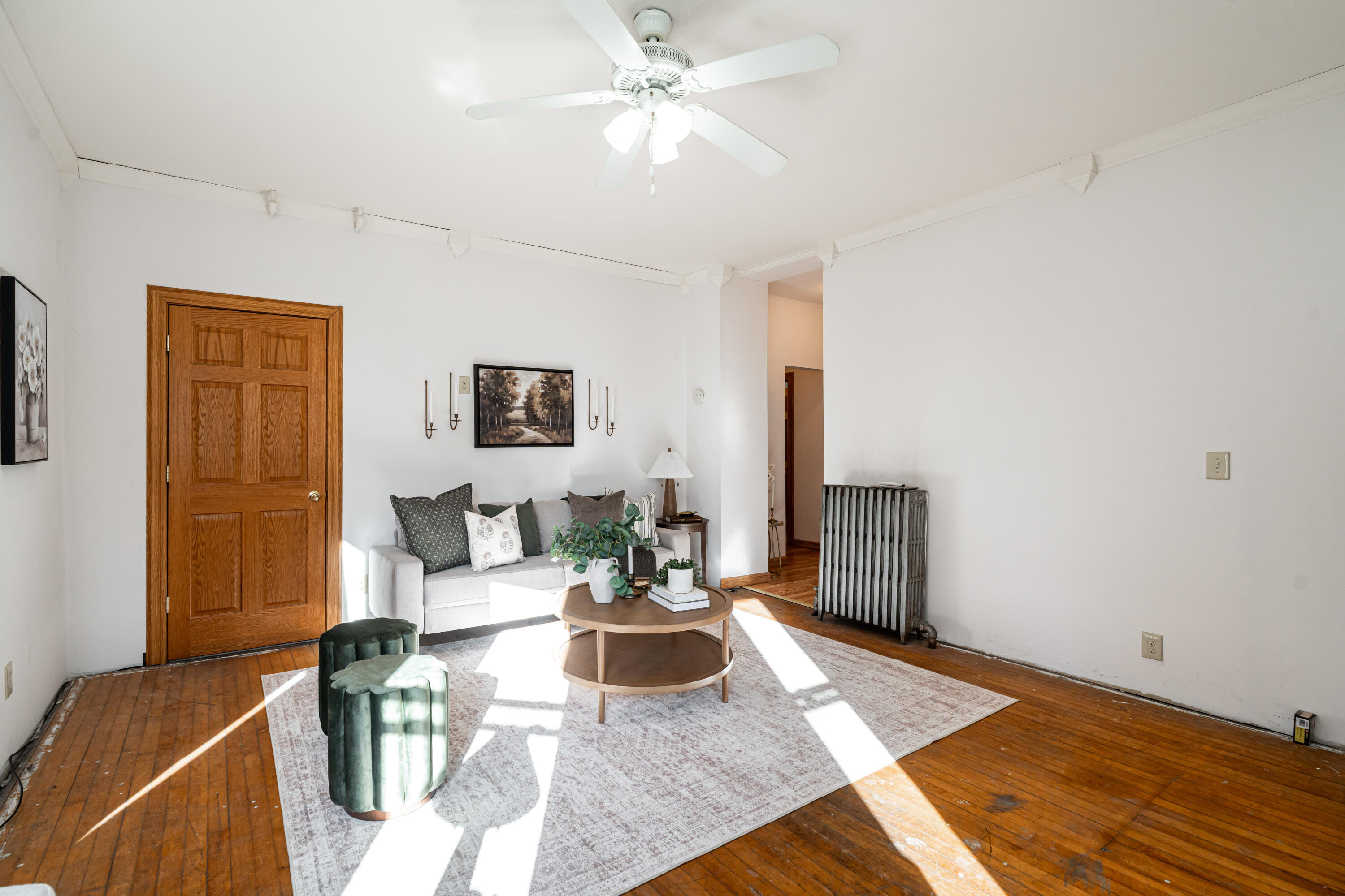Living room with a gray sofa, round coffee table, ceiling fan, and warm hardwood floors.