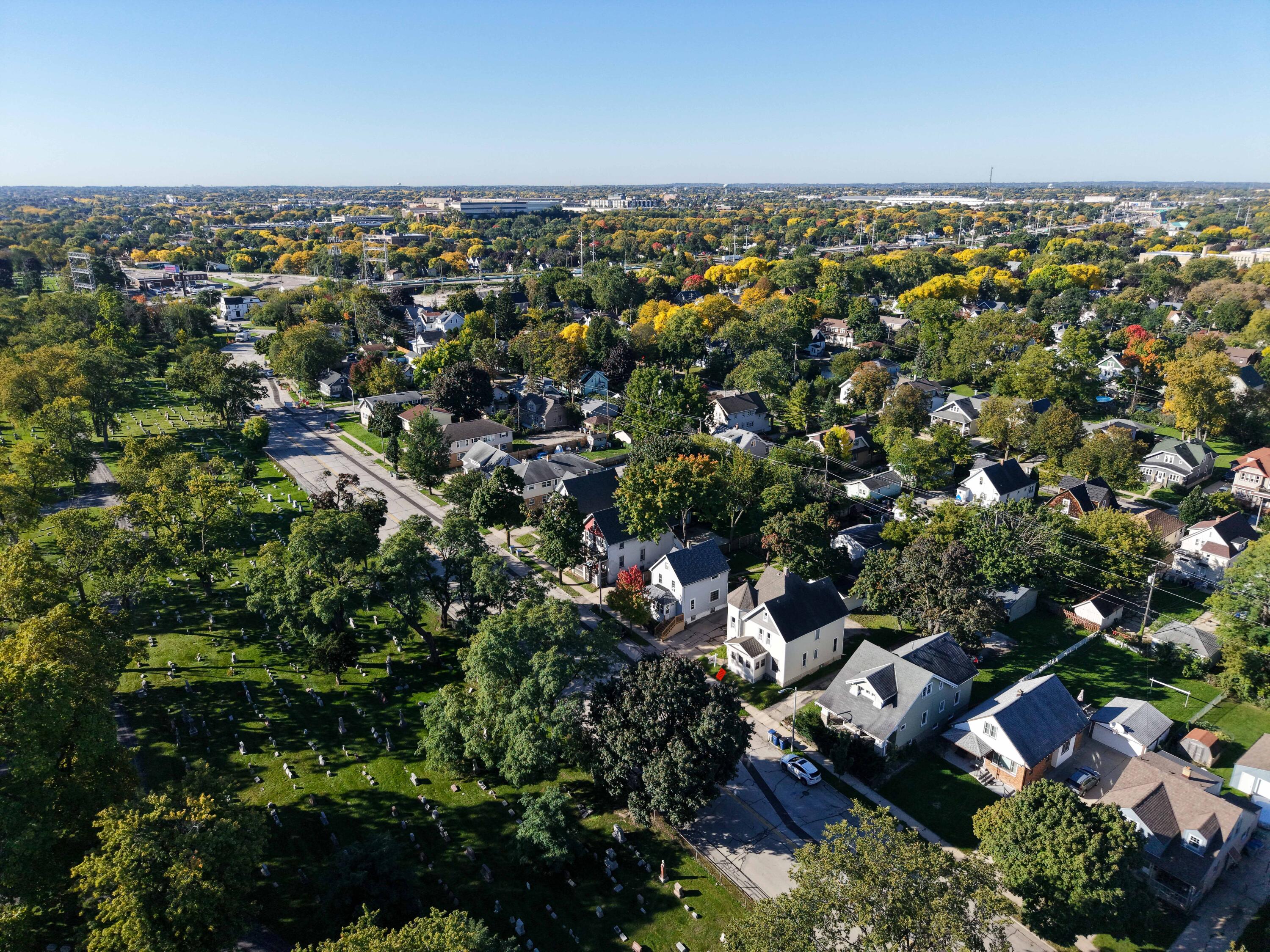 Aerial view of homes beside a cemetery, with tree-lined streets and autumn foliage.