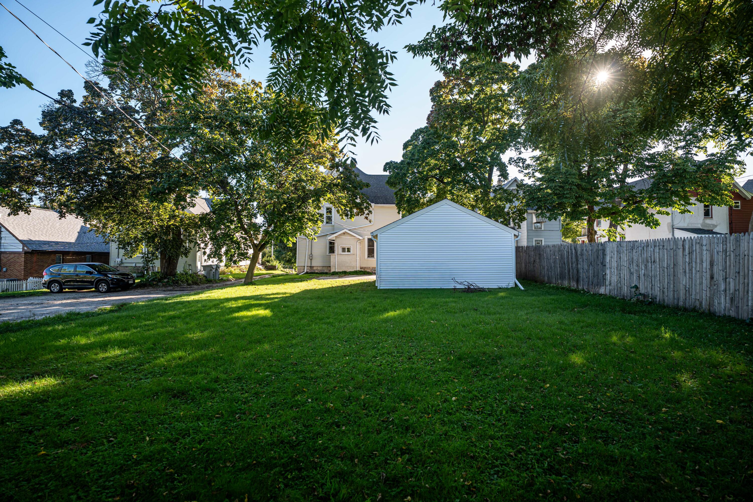Grassy backyard with mature trees, a detached light-blue garage, and wooden privacy fence.