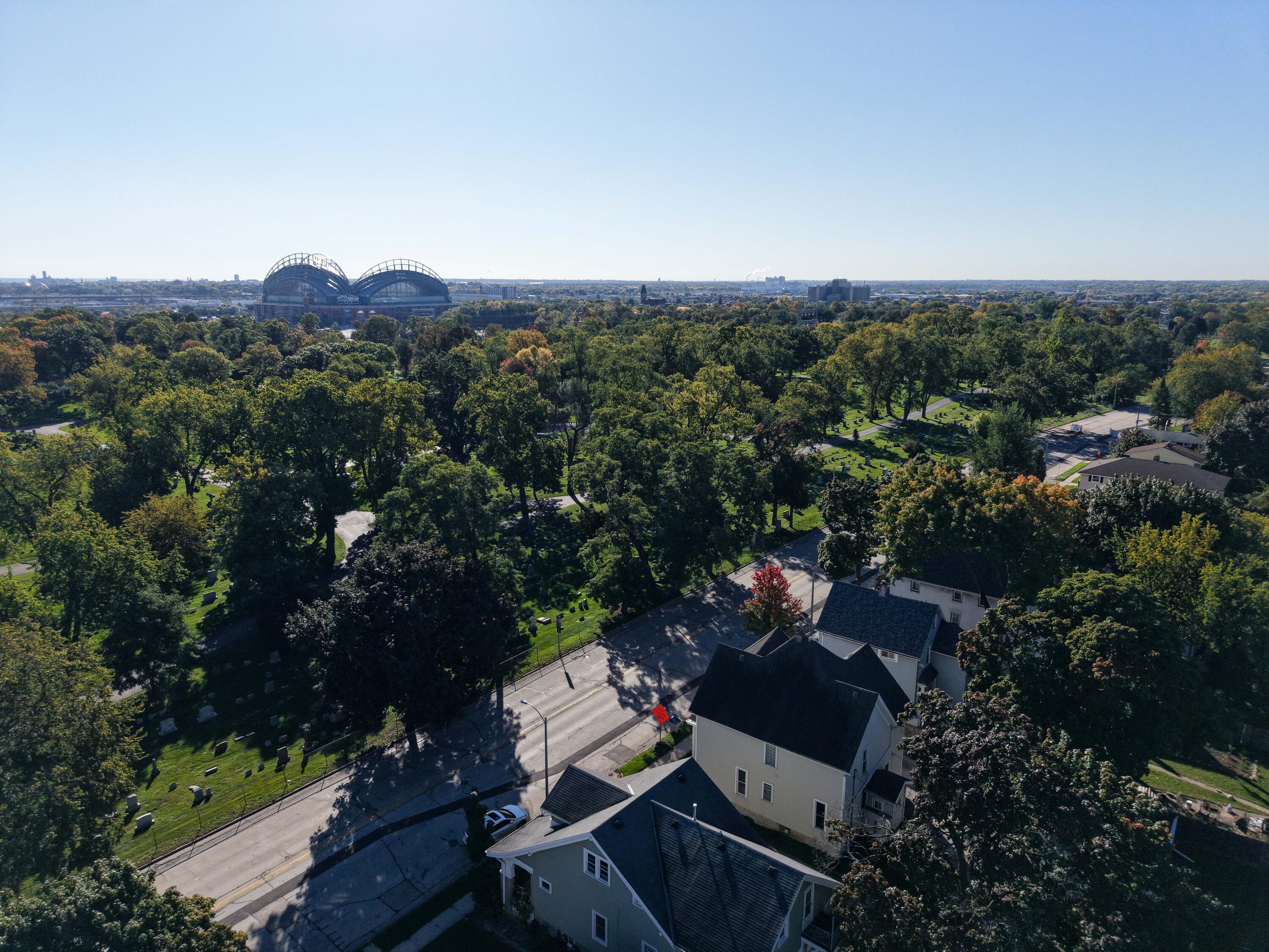 Aerial view of a tree-filled cemetery, nearby homes, and a domed stadium on the horizon.