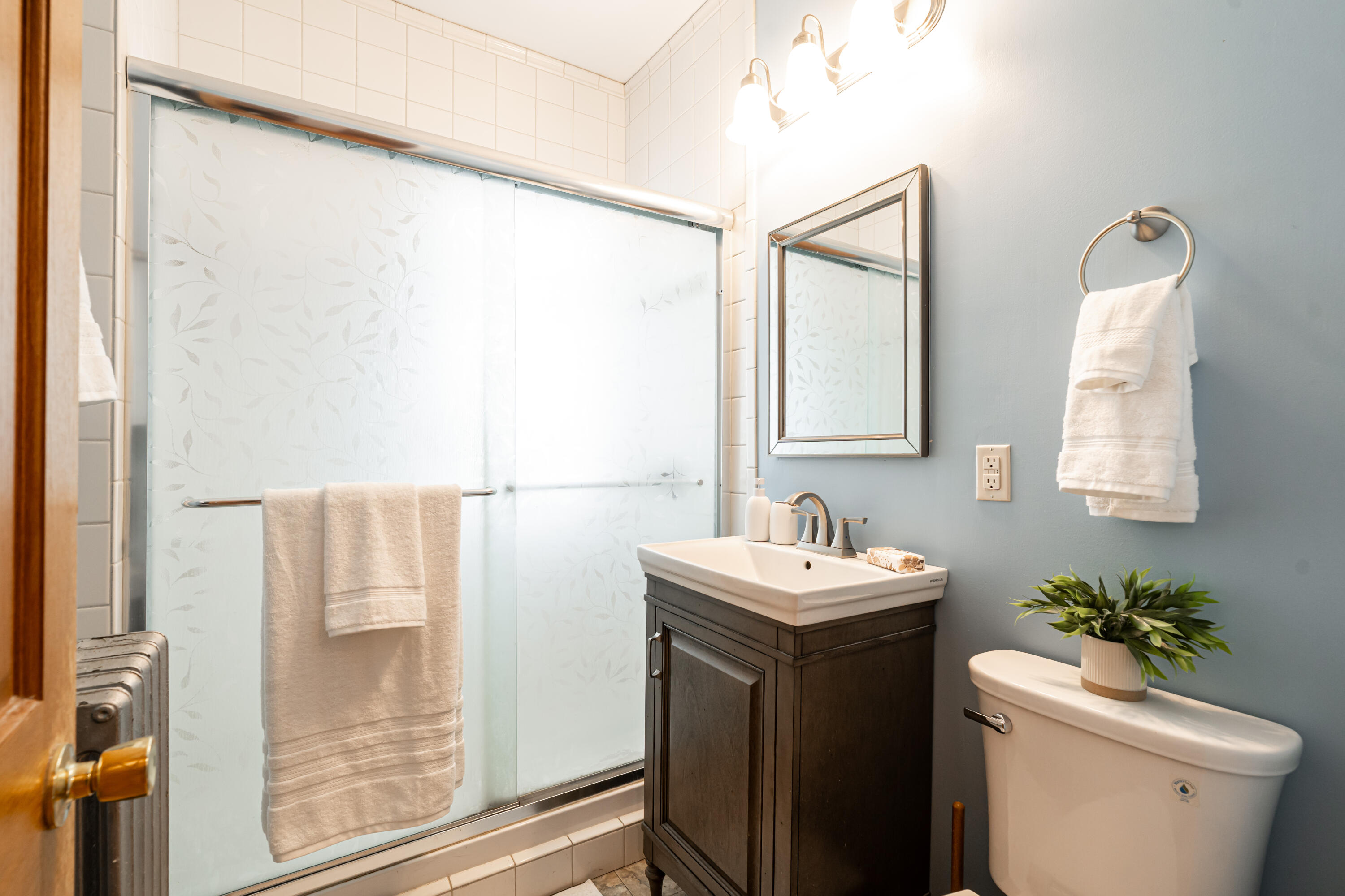 Bathroom with a leaf-patterned glass shower, dark wood vanity, and blue-gray wall.