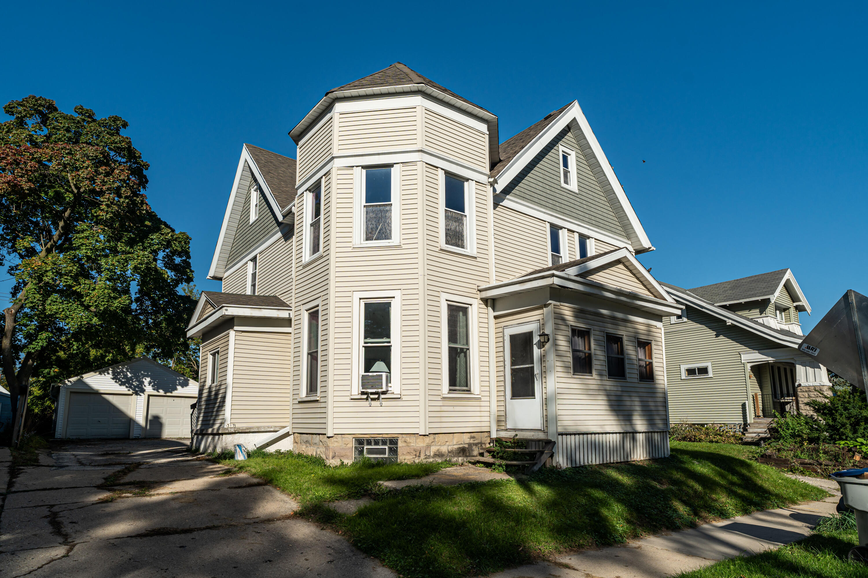 Cream-sided multi-story house with a turret, gray-green gables, and a detached garage.