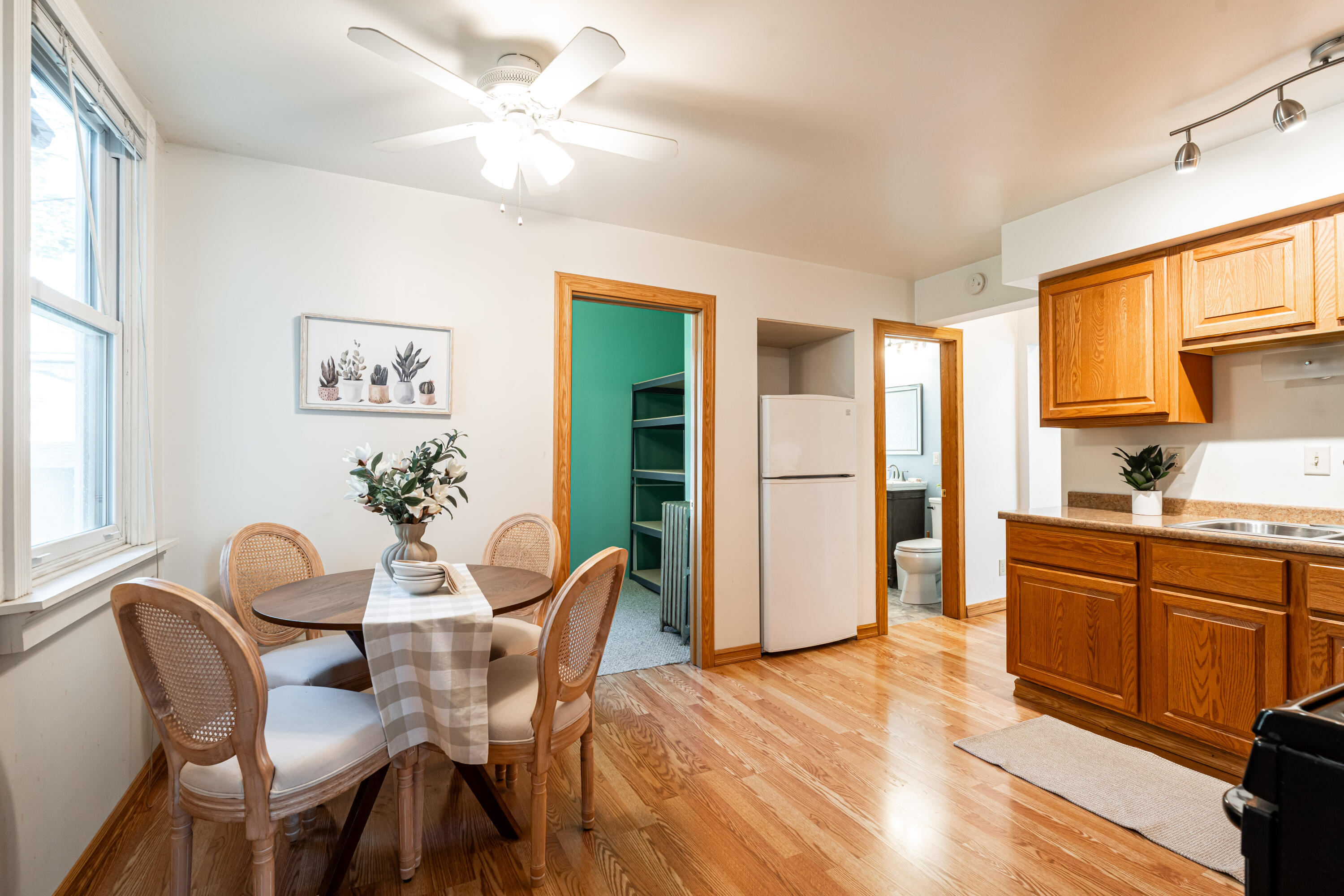 Kitchen and dining area with wood cabinets, hardwood floors, and a round table beside tall windows.