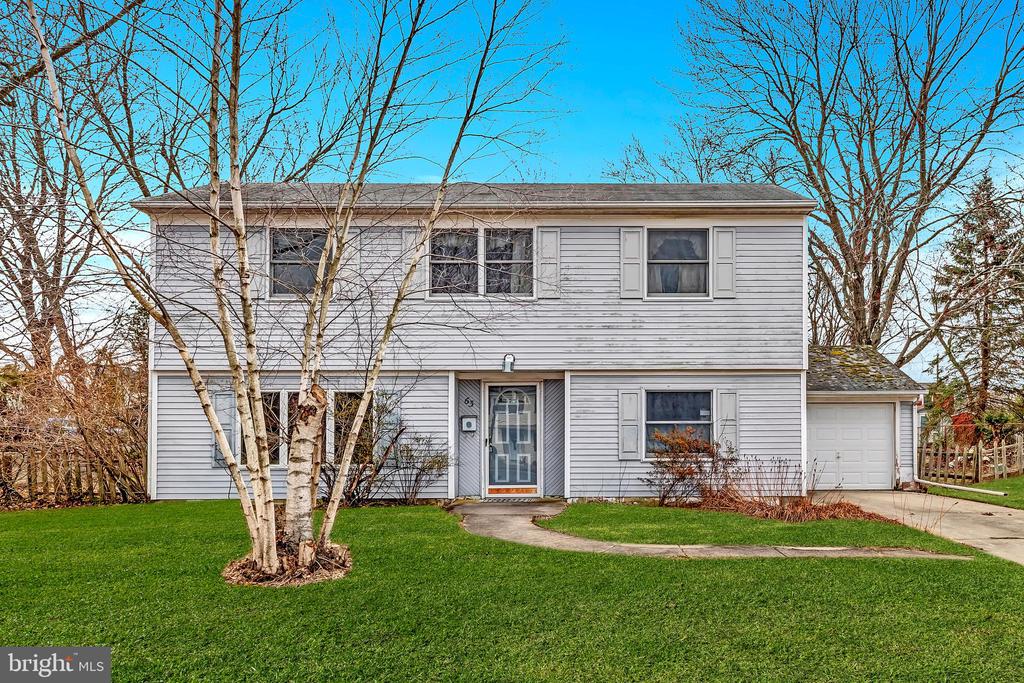 Two-story gray-sided house with an attached garage, green lawn, and leafless trees.