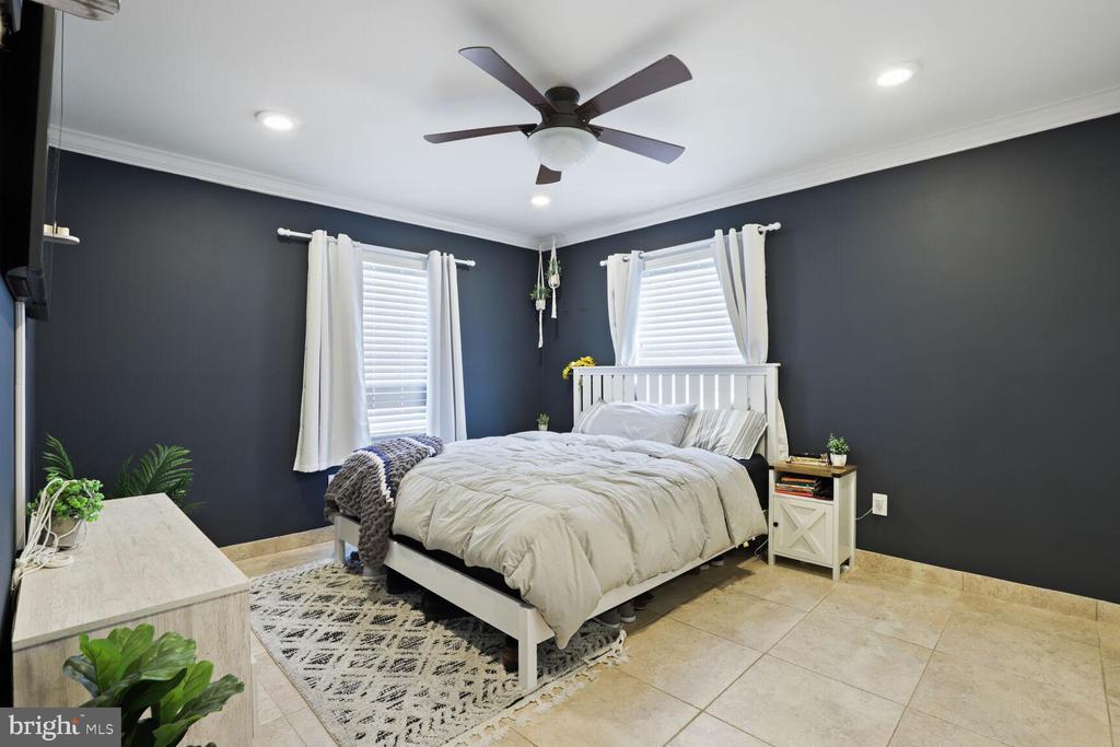 Bedroom with charcoal walls, white bedding, two curtained windows, and a ceiling fan.